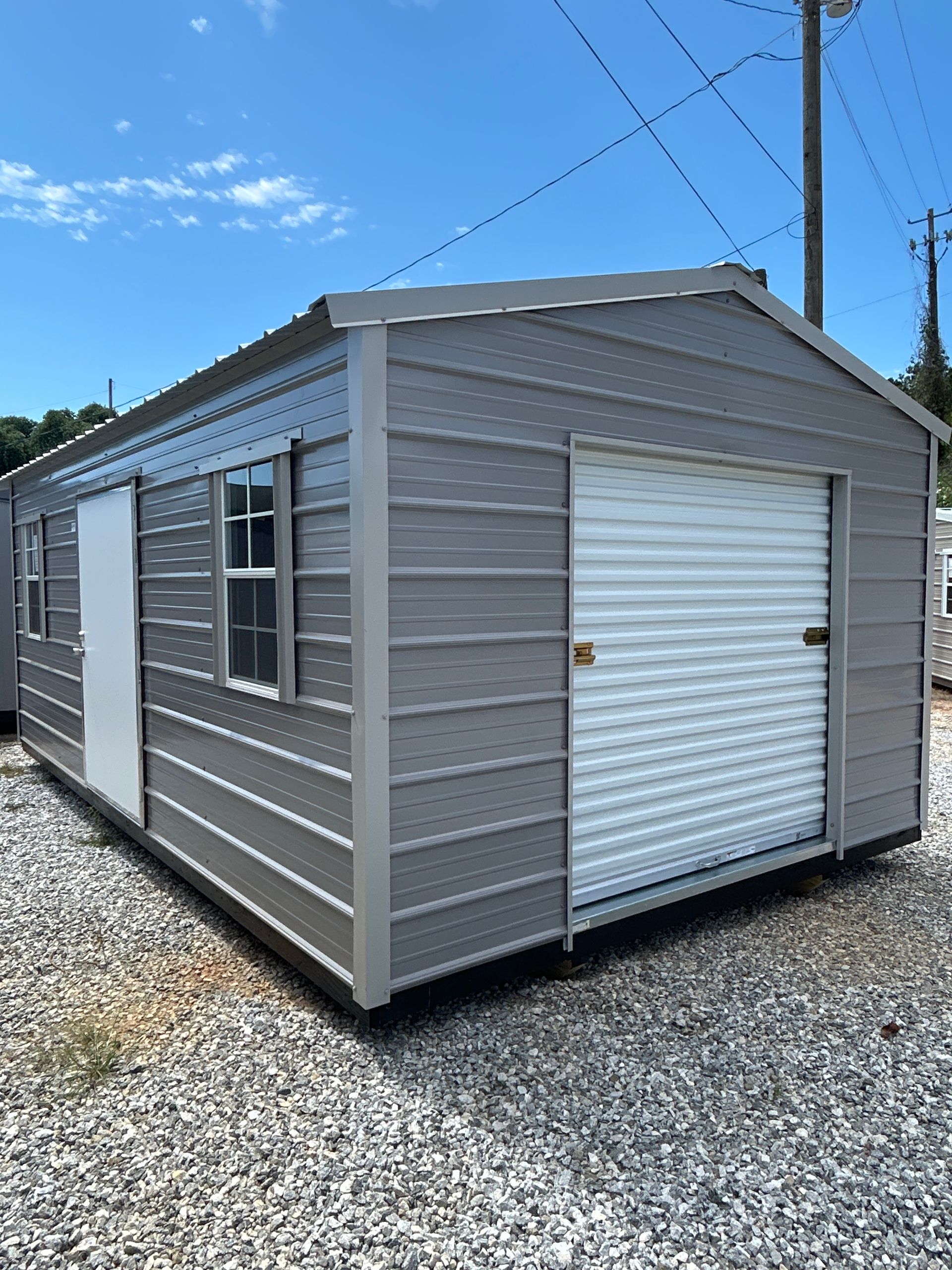 Gray metal shed with a roll-up garage door, a white door, and a window, set on gravel.