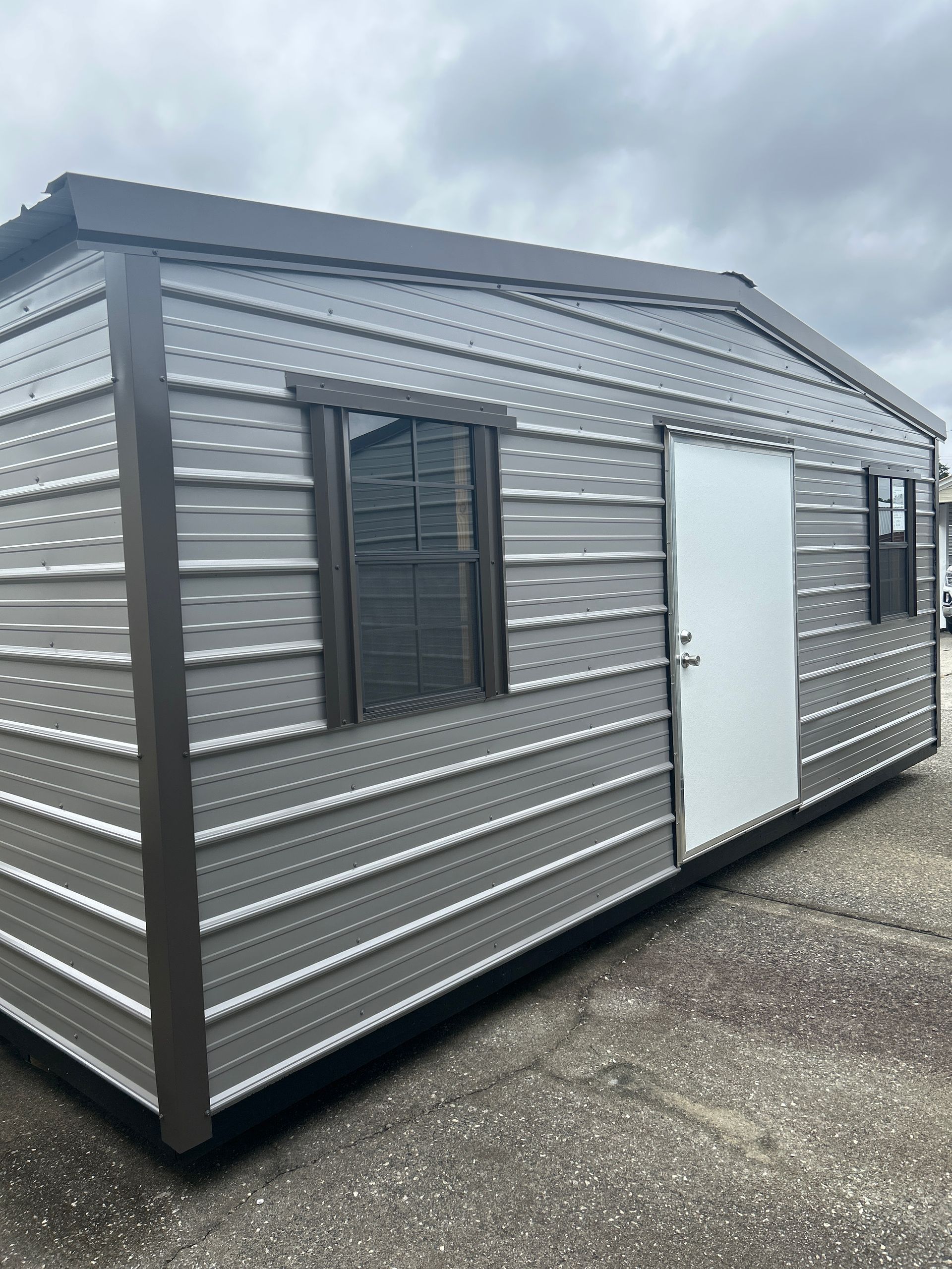 Gray metal shed with a brown trim, white door, and two windows.