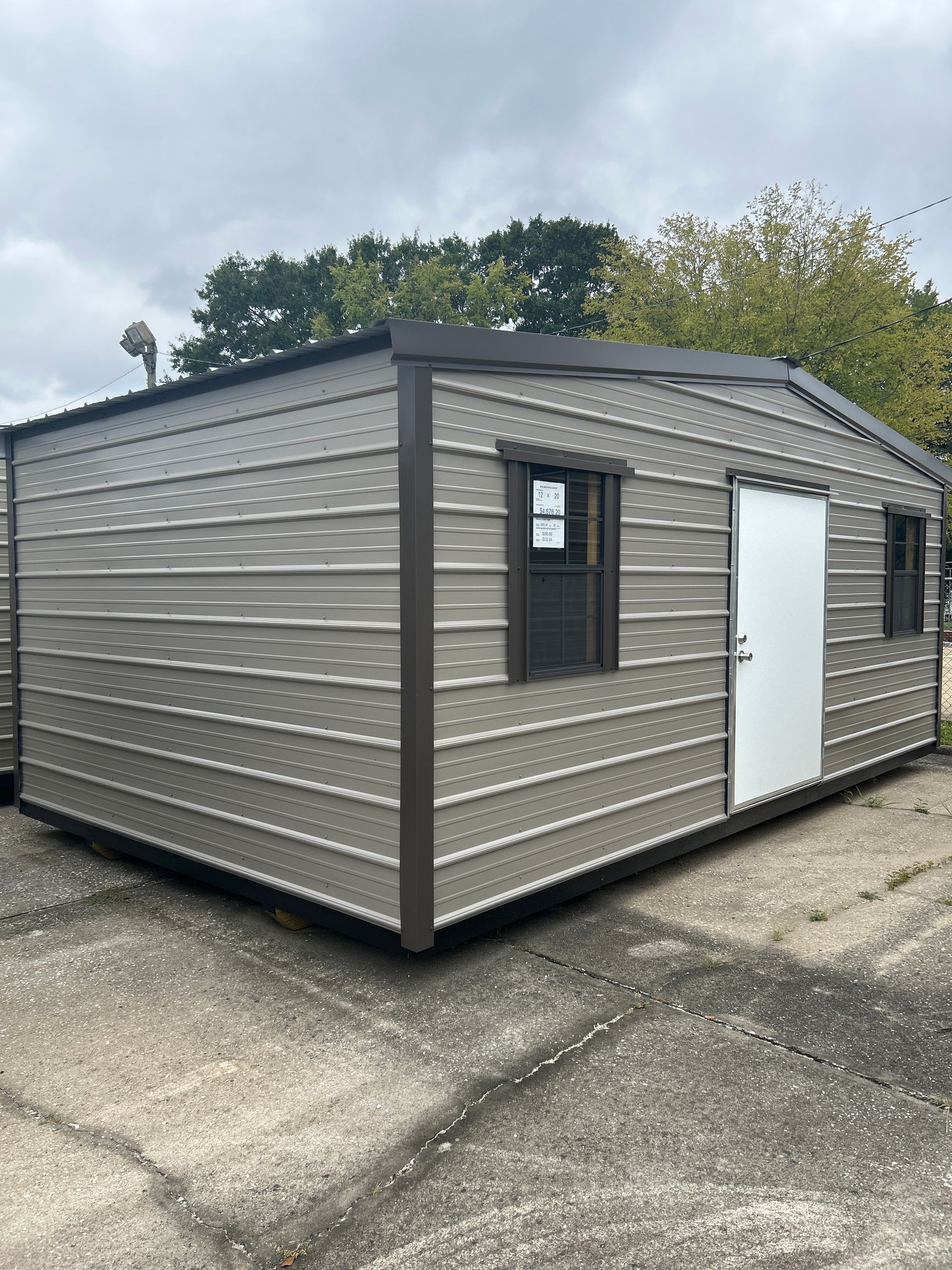 Tan metal shed with brown trim, door, and windows, outdoors.
