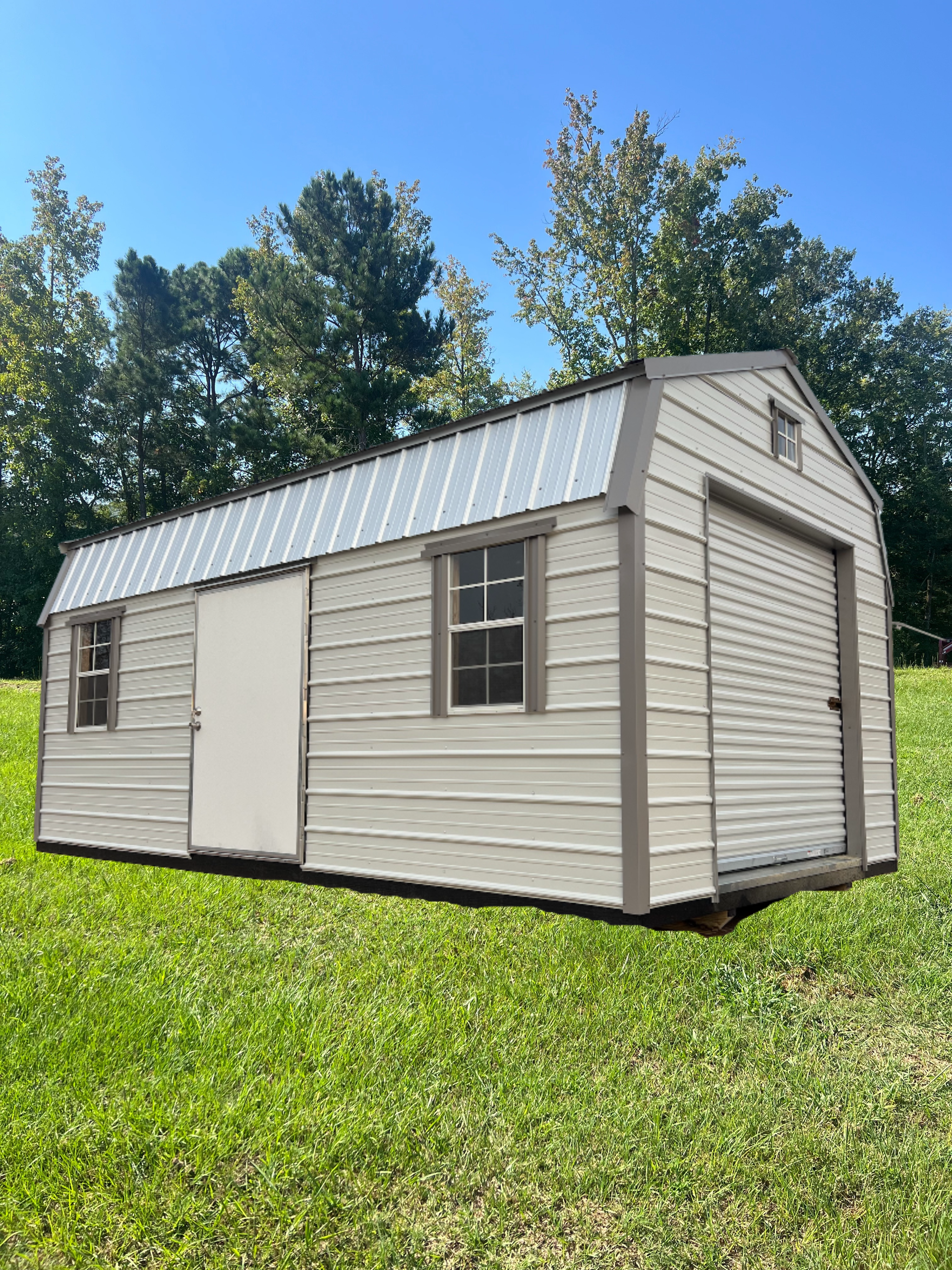 Light gray shed with a metal roof and a garage door on a grassy lawn.