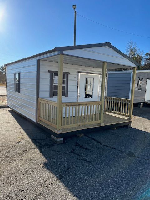 Small white prefabricated cabin with a porch under a bright sky.