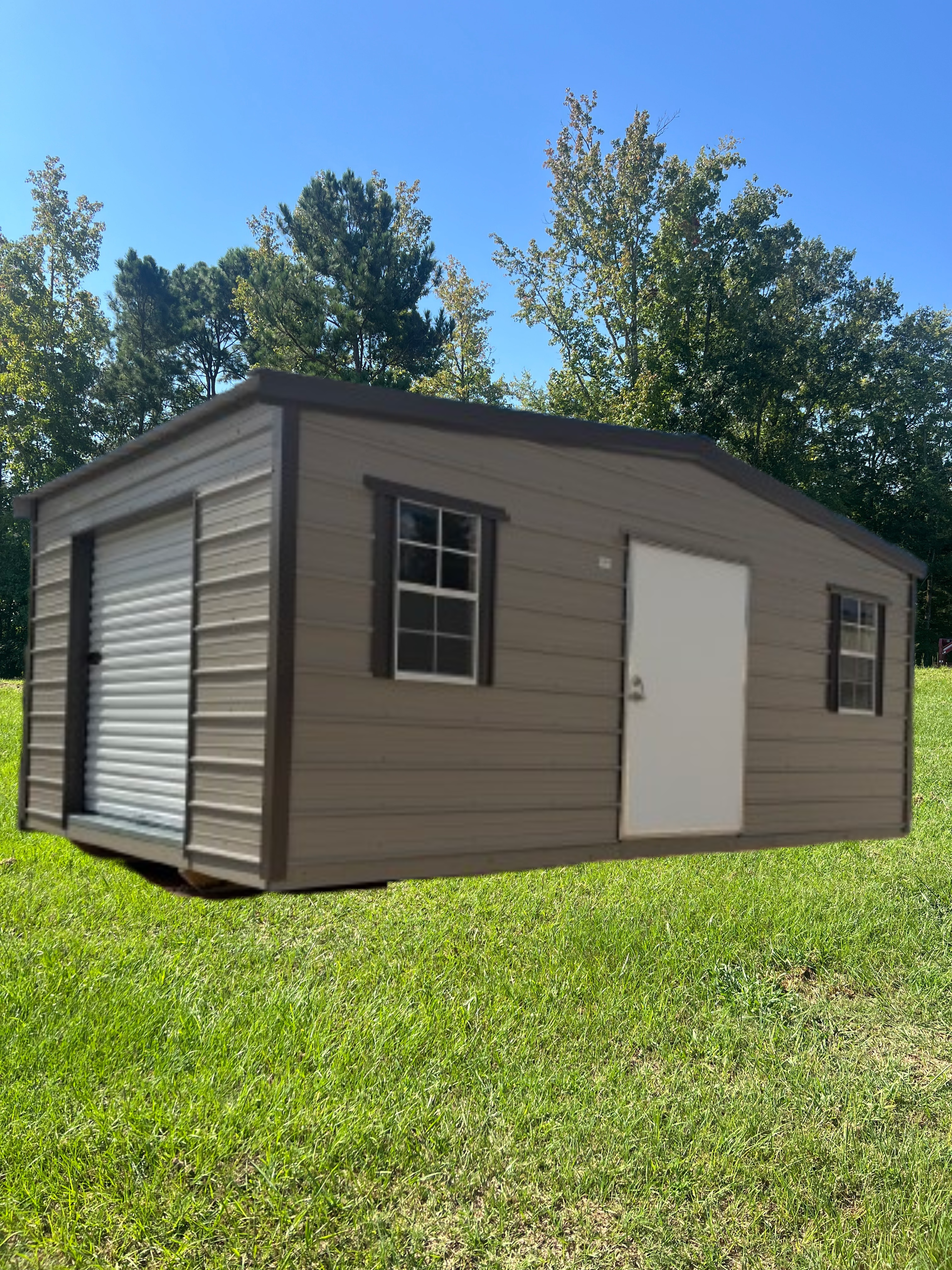 Tan storage shed with a roll-up side door, a standard door, and two windows, set on a grassy lawn under a blue sky.