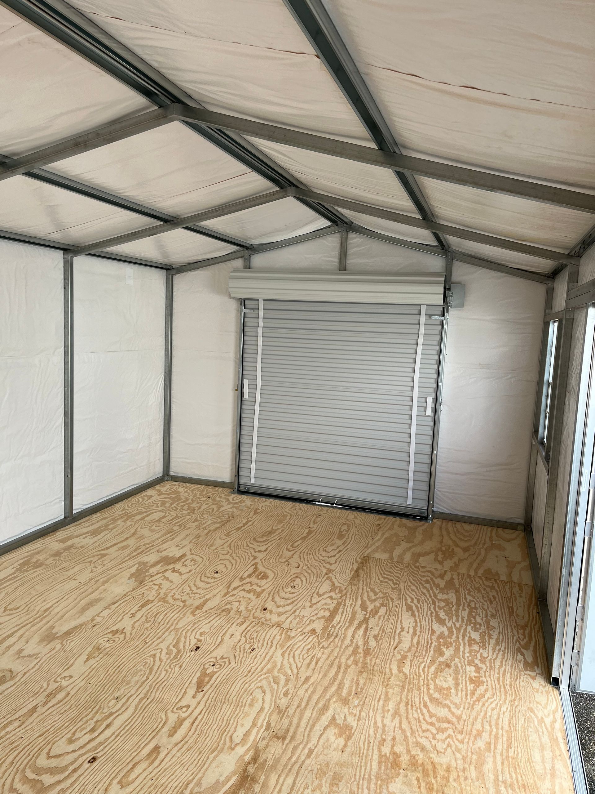 Empty metal storage shed with plywood floor and a closed roll-up door