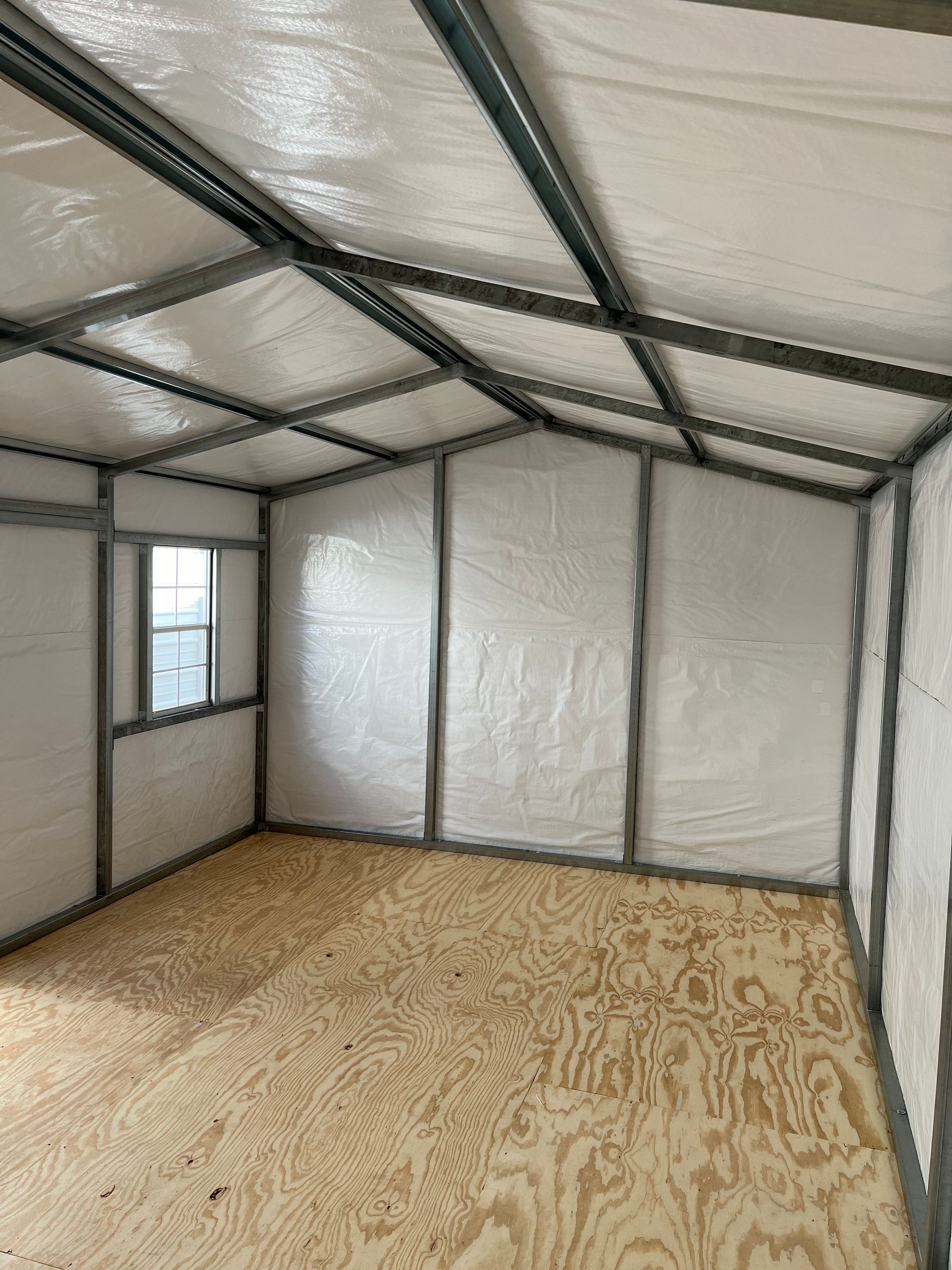 Empty insulated room with plywood floor, metal frame roof, and a small window.