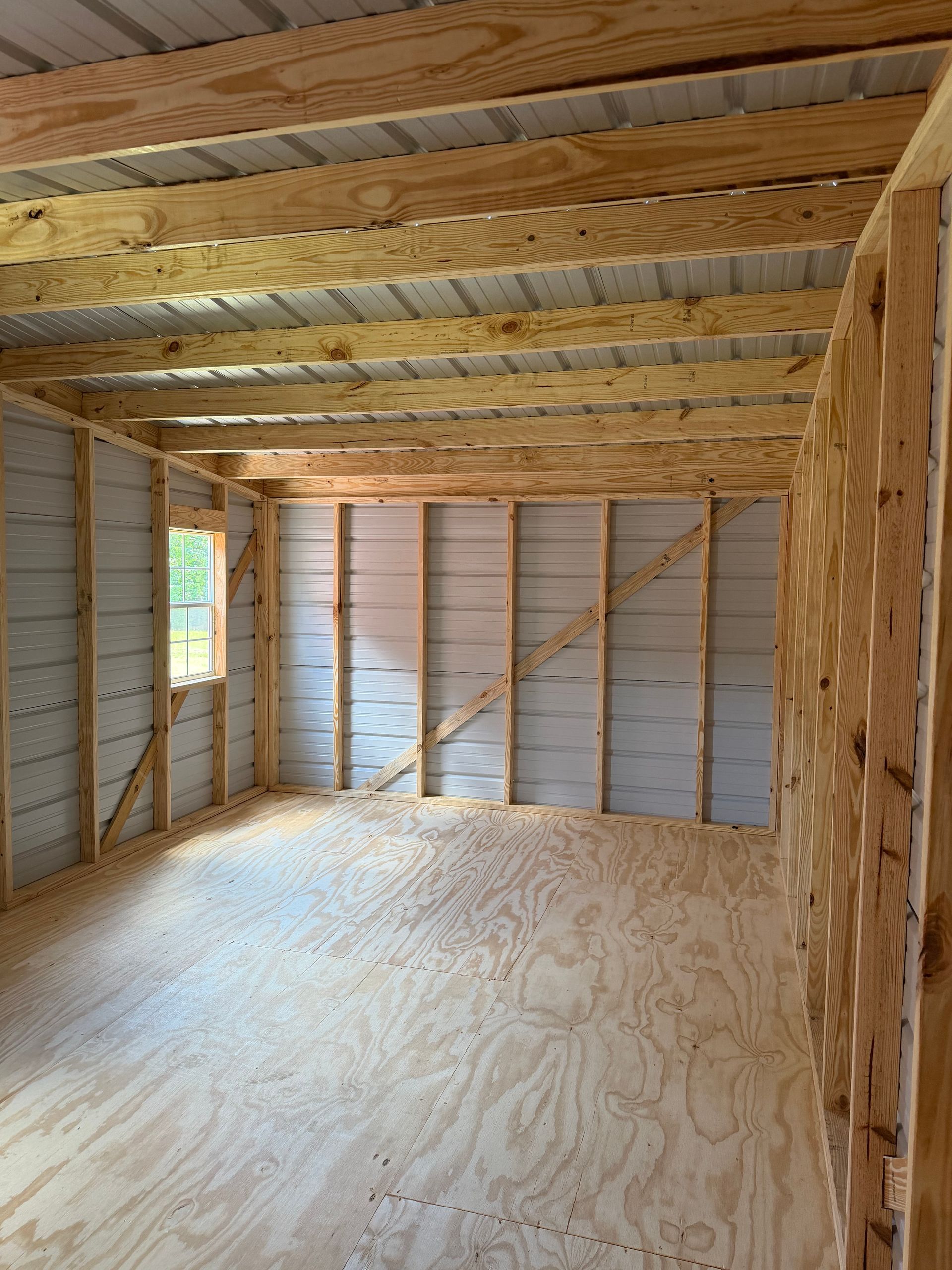 Interior of an unfinished wooden room with exposed beams, plywood floor, and insulation between wall studs.