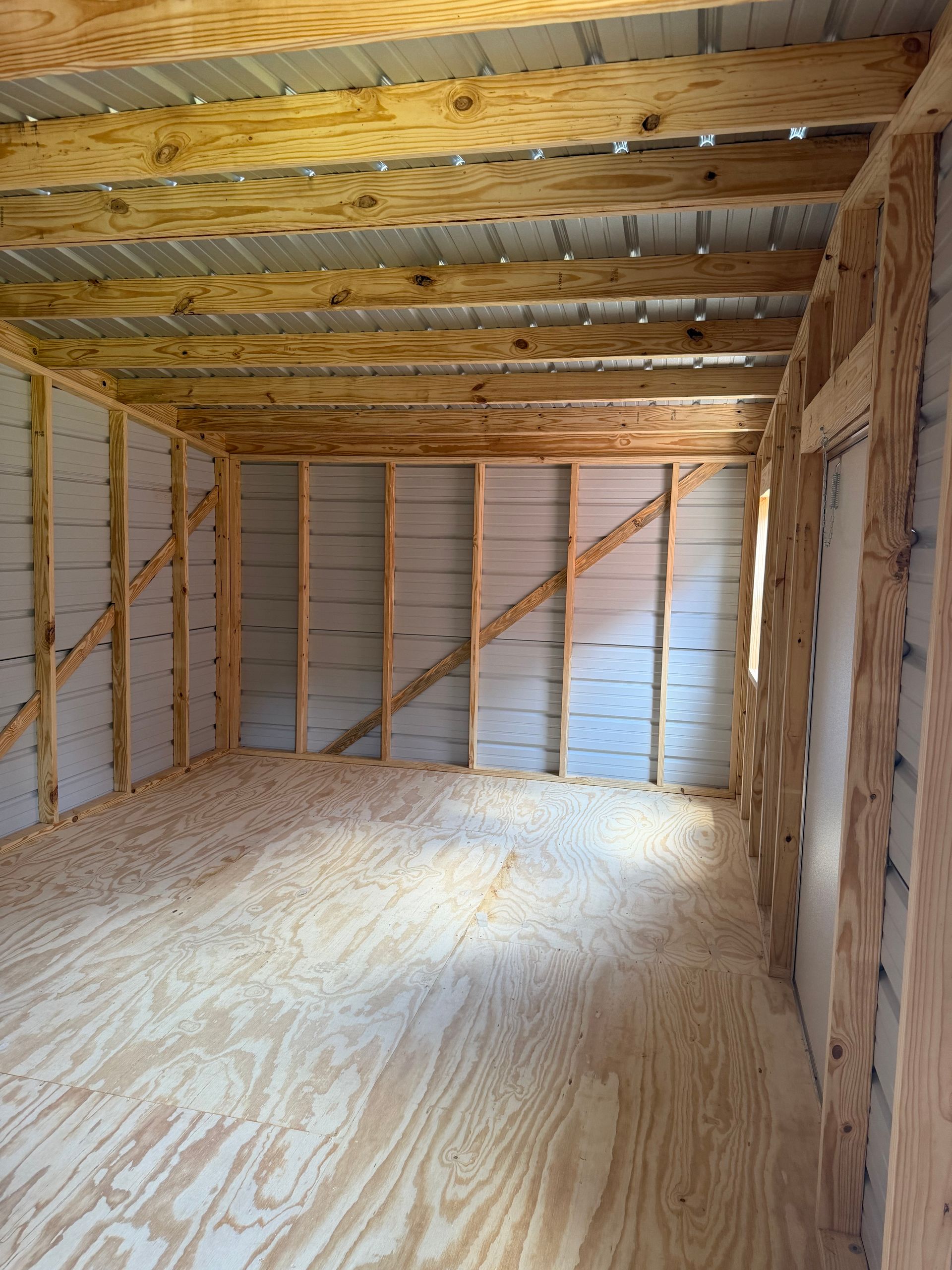Empty unfinished wooden room with exposed studs, plywood floor, and insulation in the ceiling.