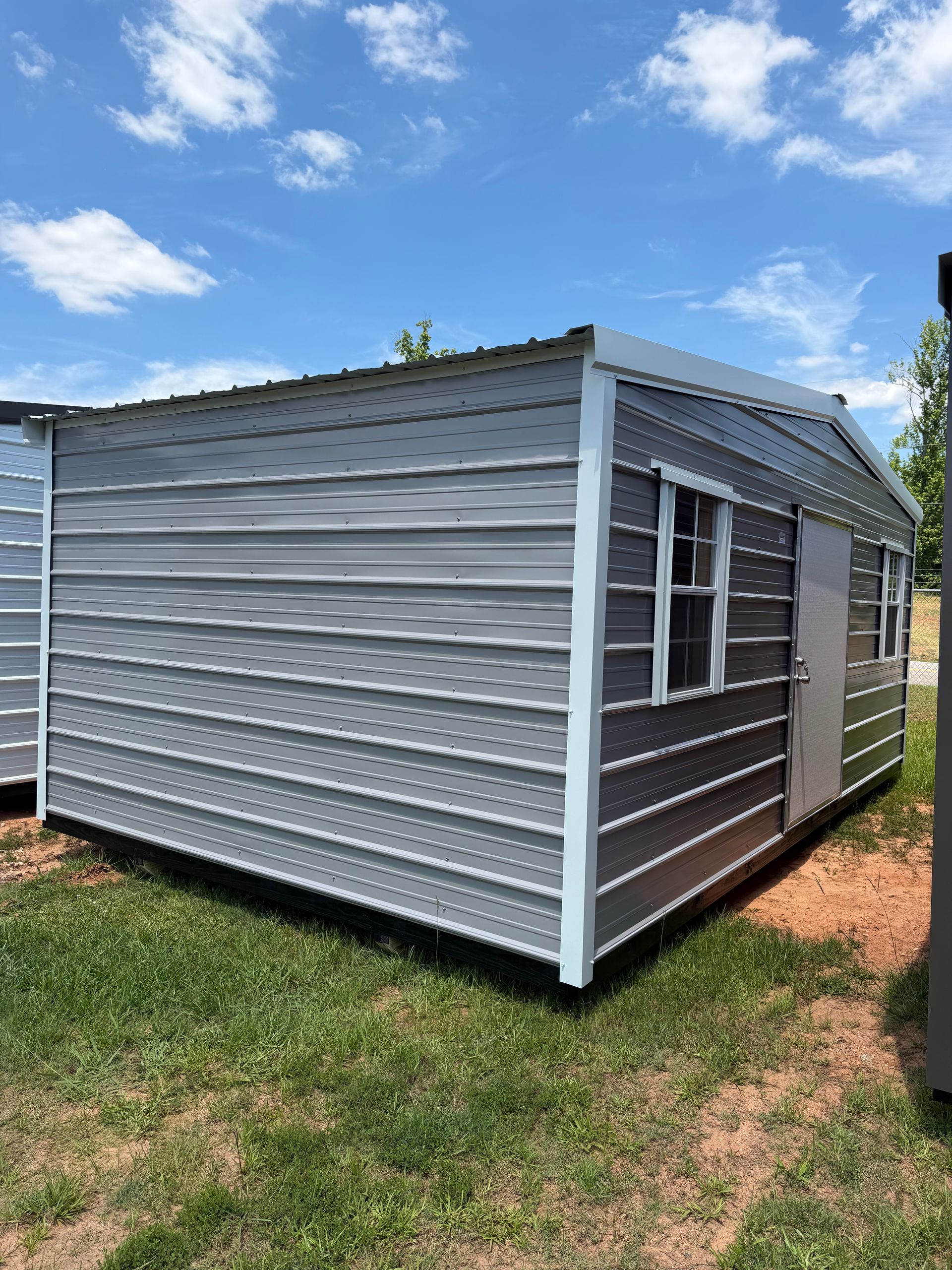 Small gray corrugated shed with white trim on a grassy yard under a blue sky
