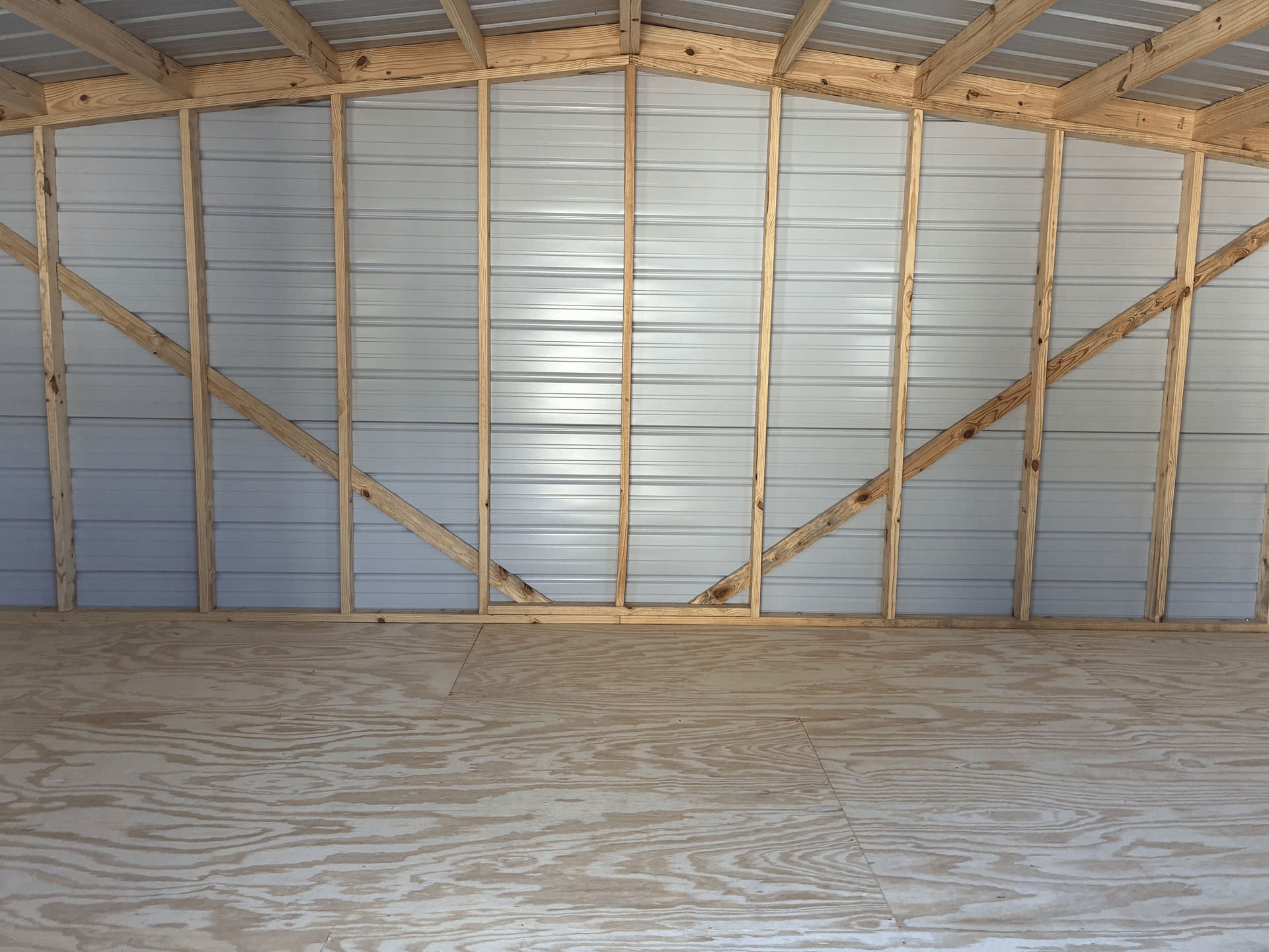 Empty unfinished garage interior with exposed wooden framing, metal siding, and plywood floor under construction
