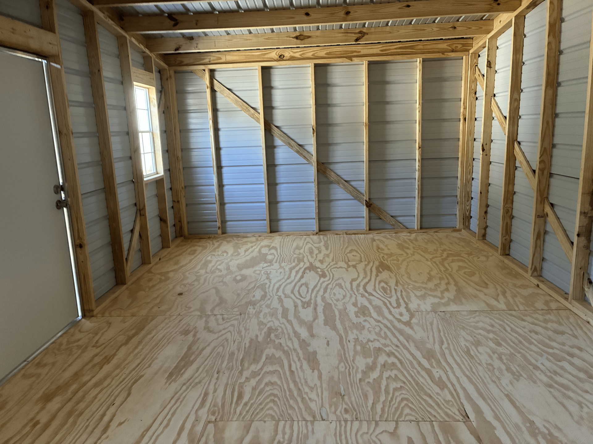 Empty unfinished room with plywood floor, exposed wooden framing, and insulated walls and ceiling