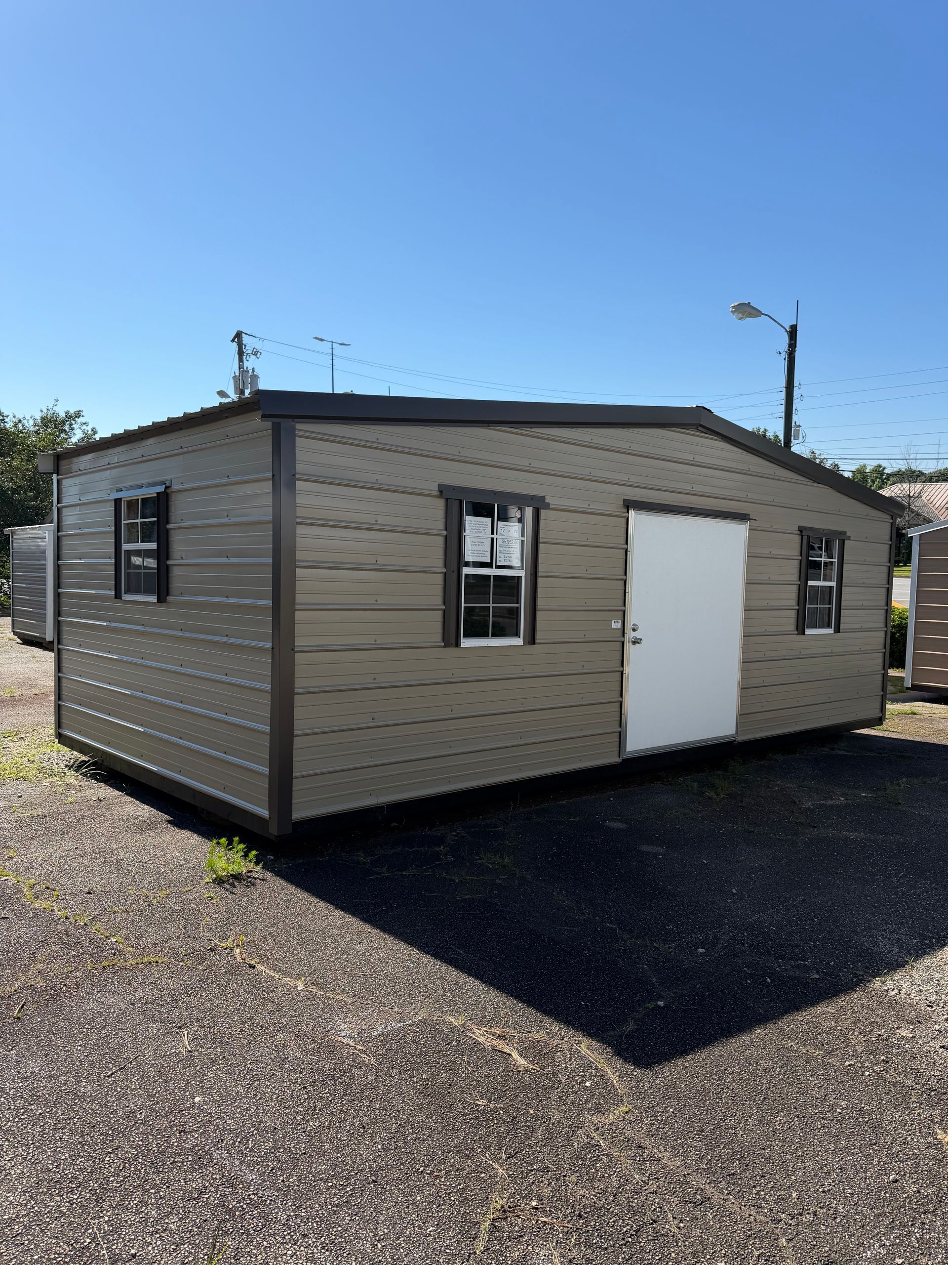 Small beige modular building with white door and windows on a gravel lot under a clear blue sky