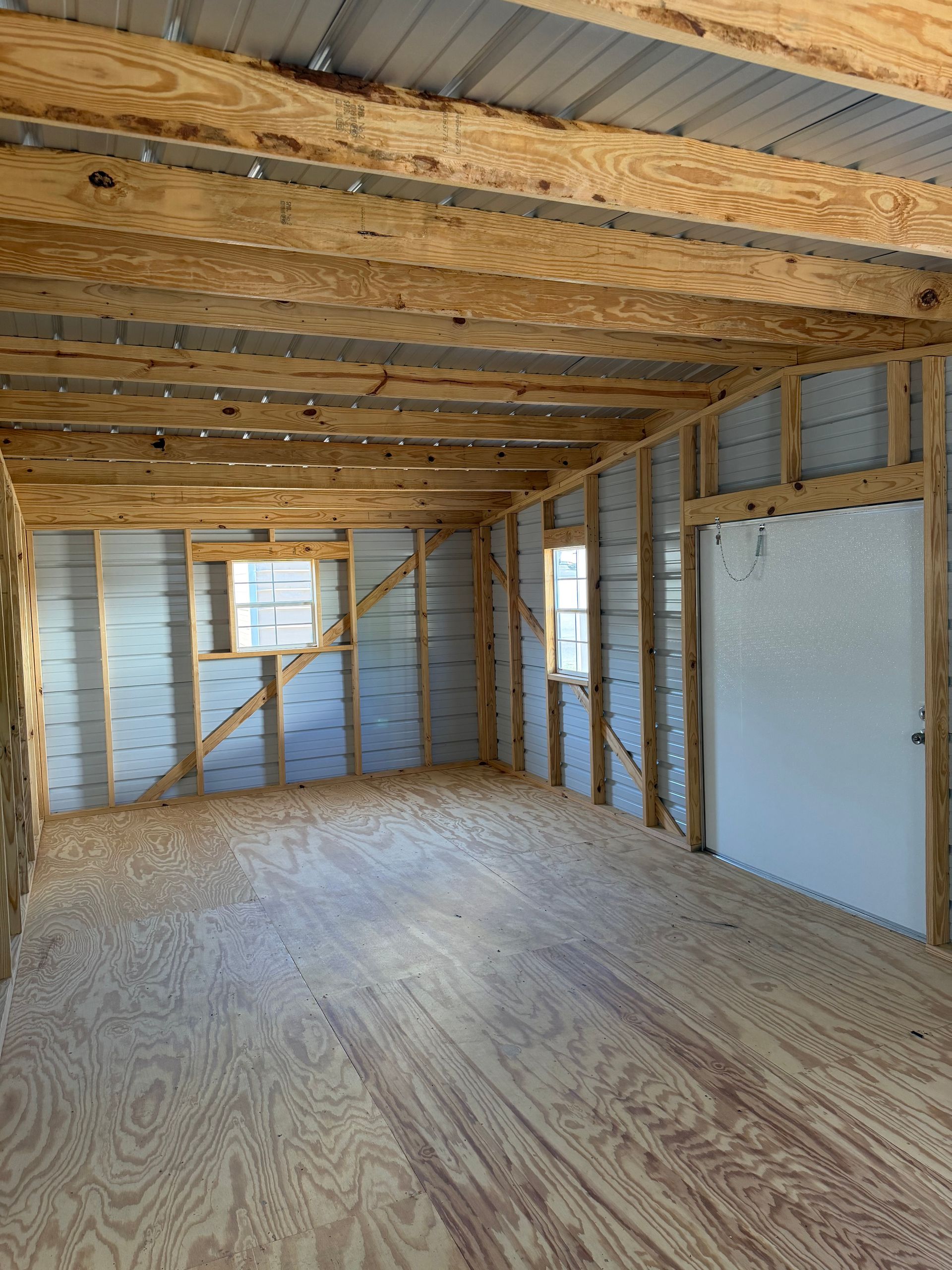 Empty unfinished room with exposed wood framing, plywood floor, and insulation panels under construction.