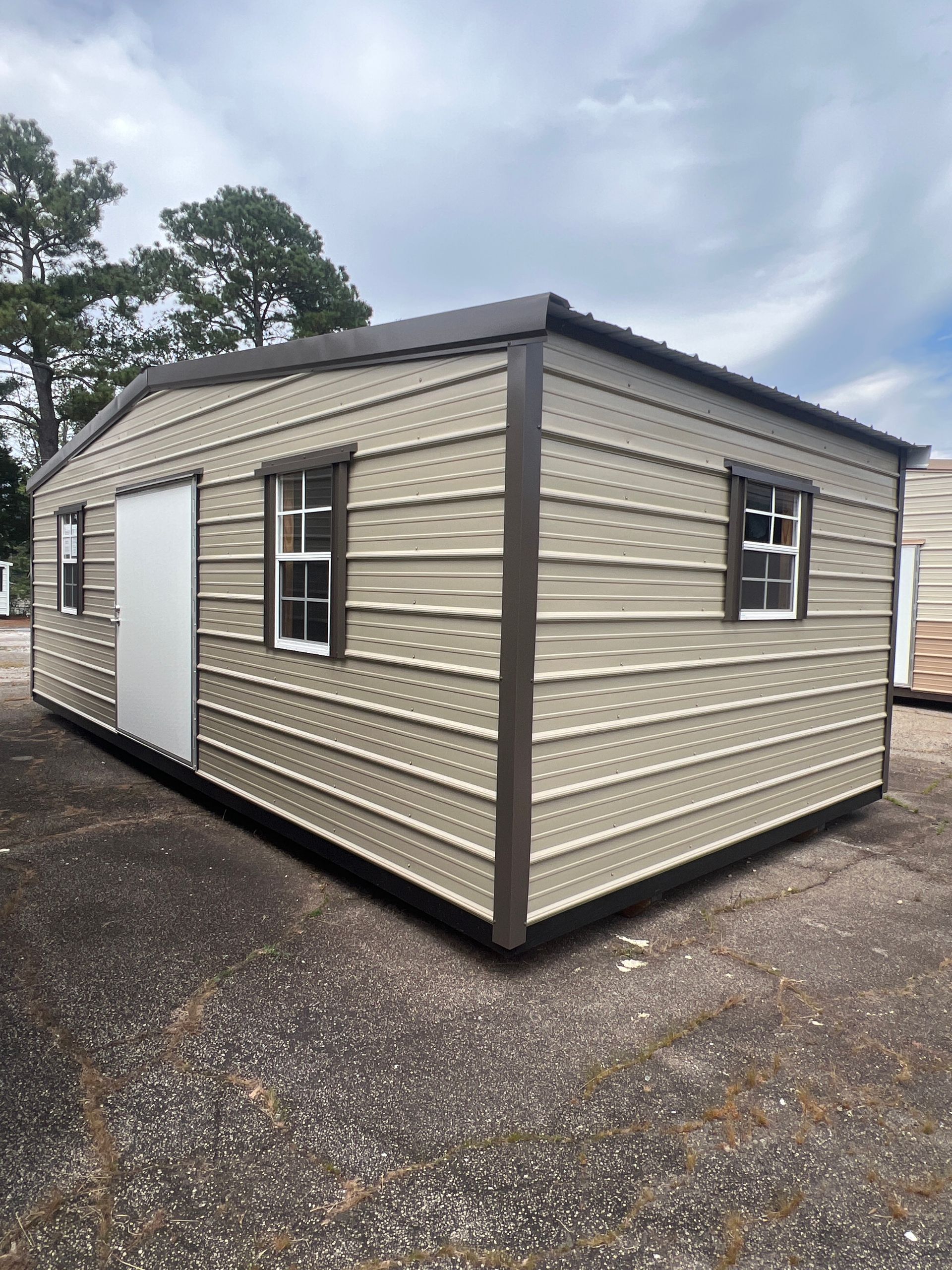 Tan metal storage building with brown trim, door, and windows, outdoors.