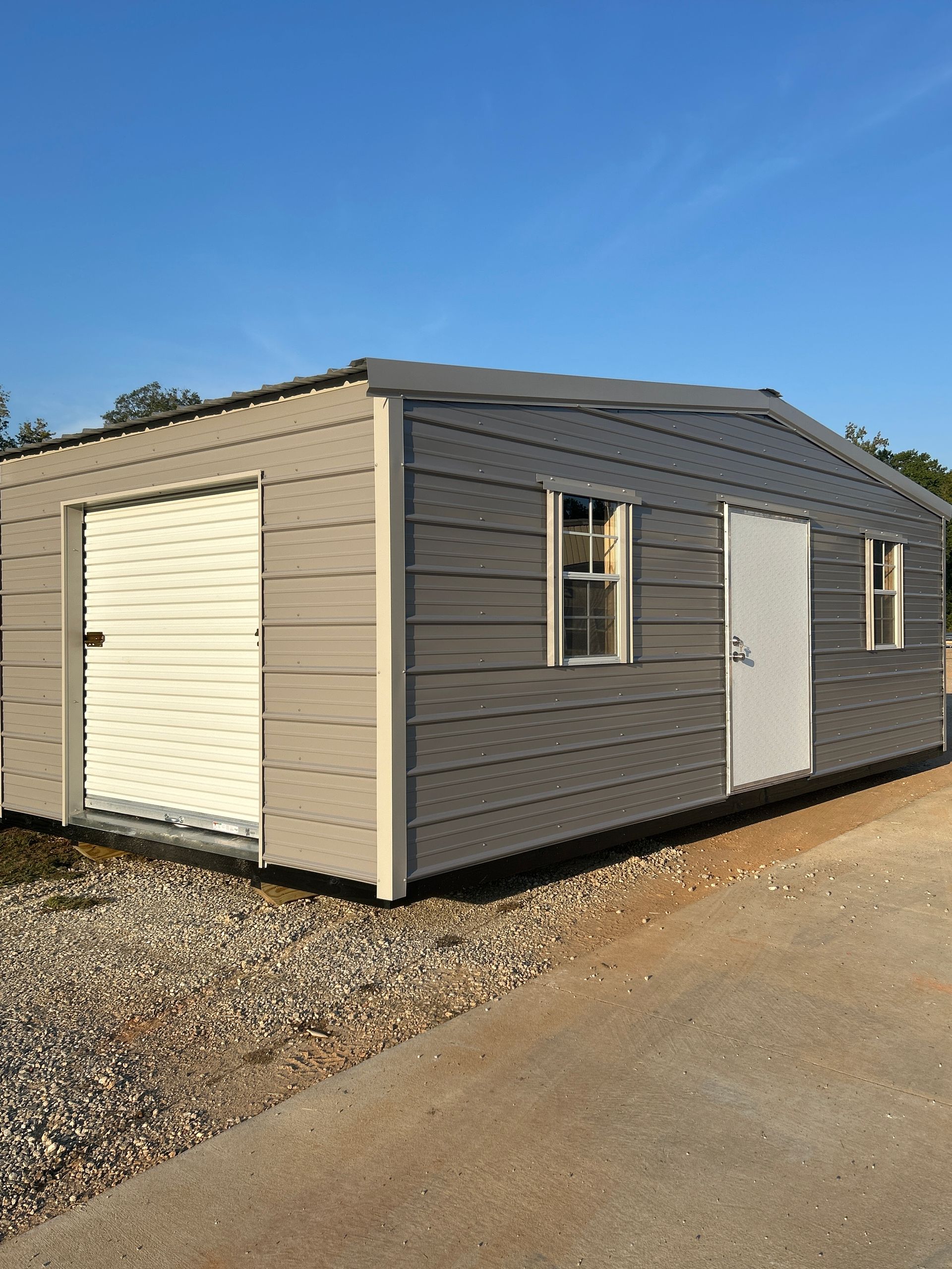 Gray metal shed with white doors and windows, set on gravel.