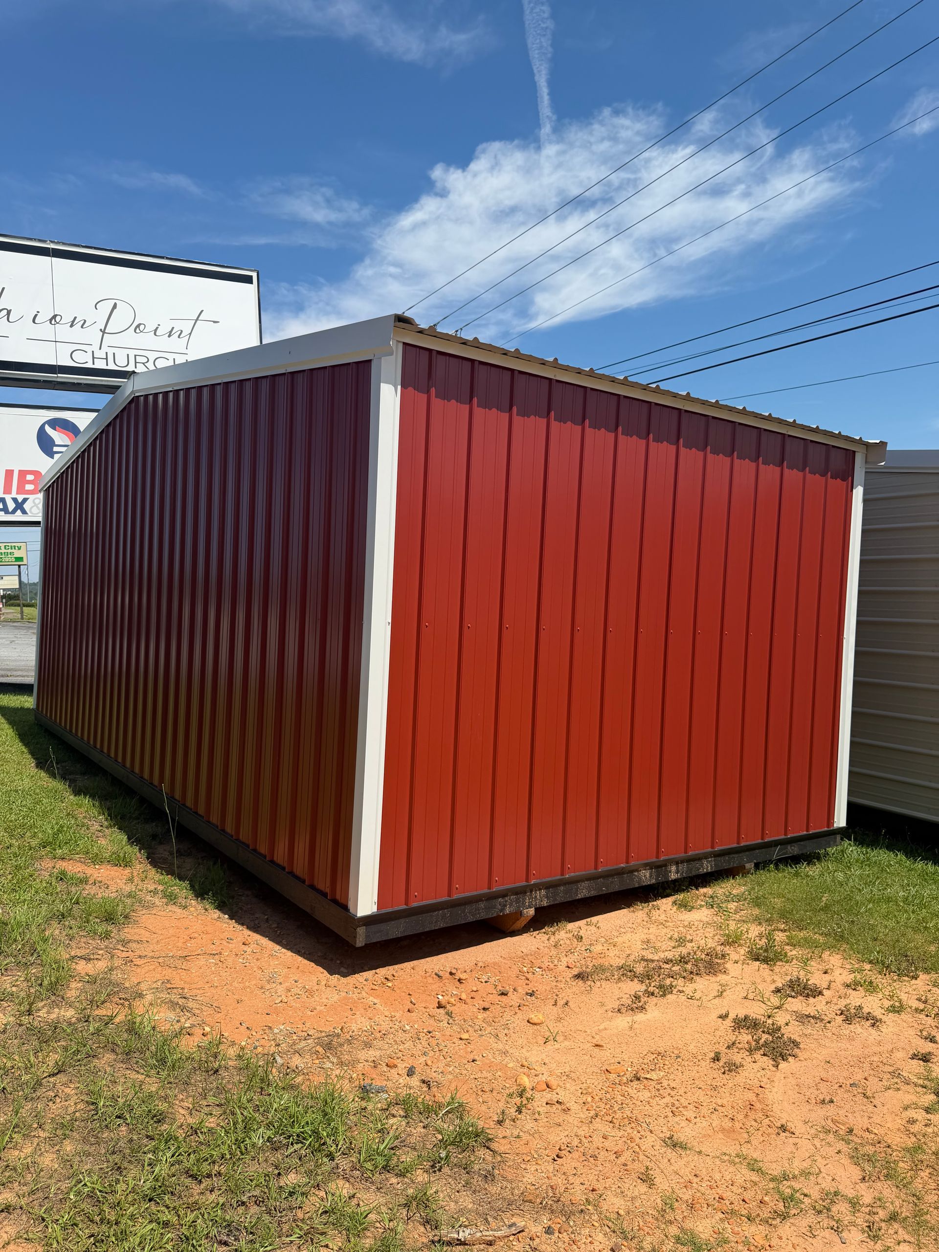 Red shipping container shed with white trim on a grassy dirt lot under a blue sky