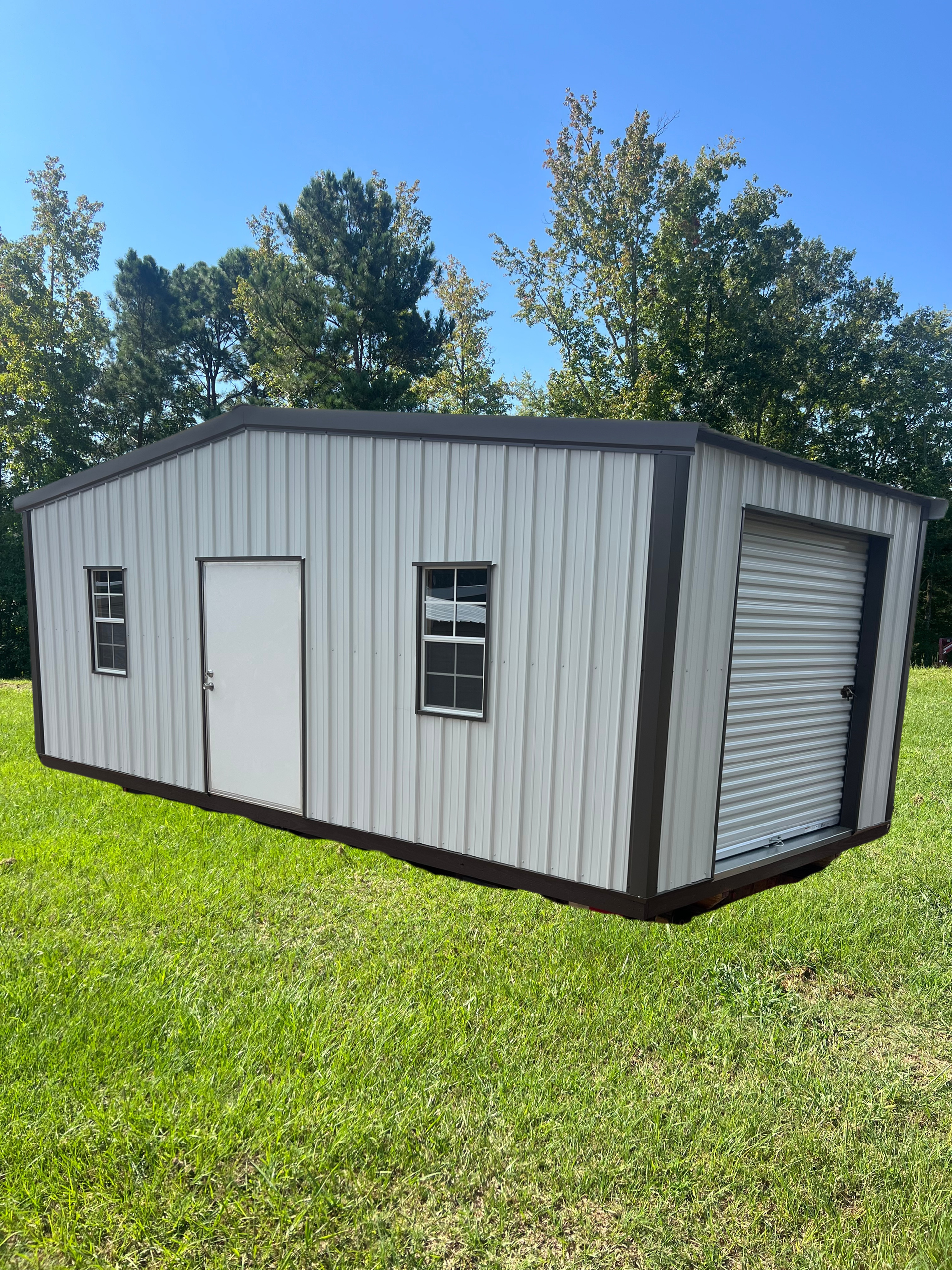Metal shed with a roll-up garage door, white door, and two windows on a grassy lawn.