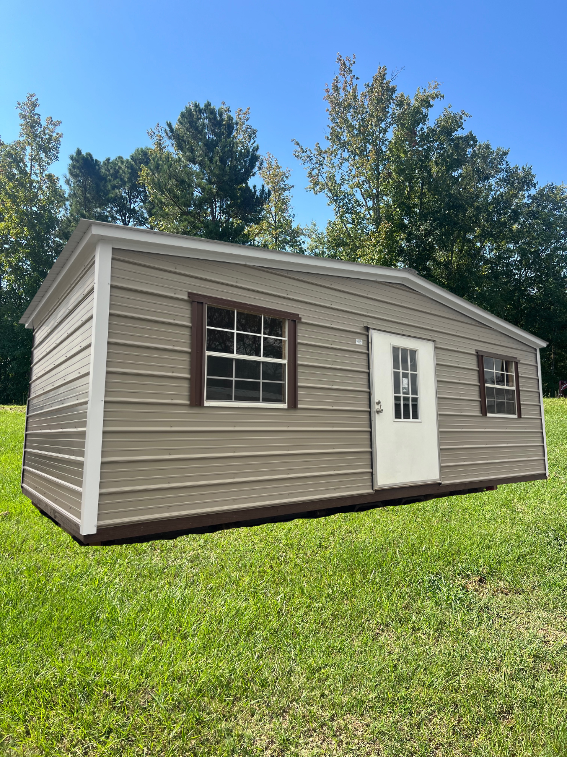 Gray metal shed with white doors and windows, set on gravel.