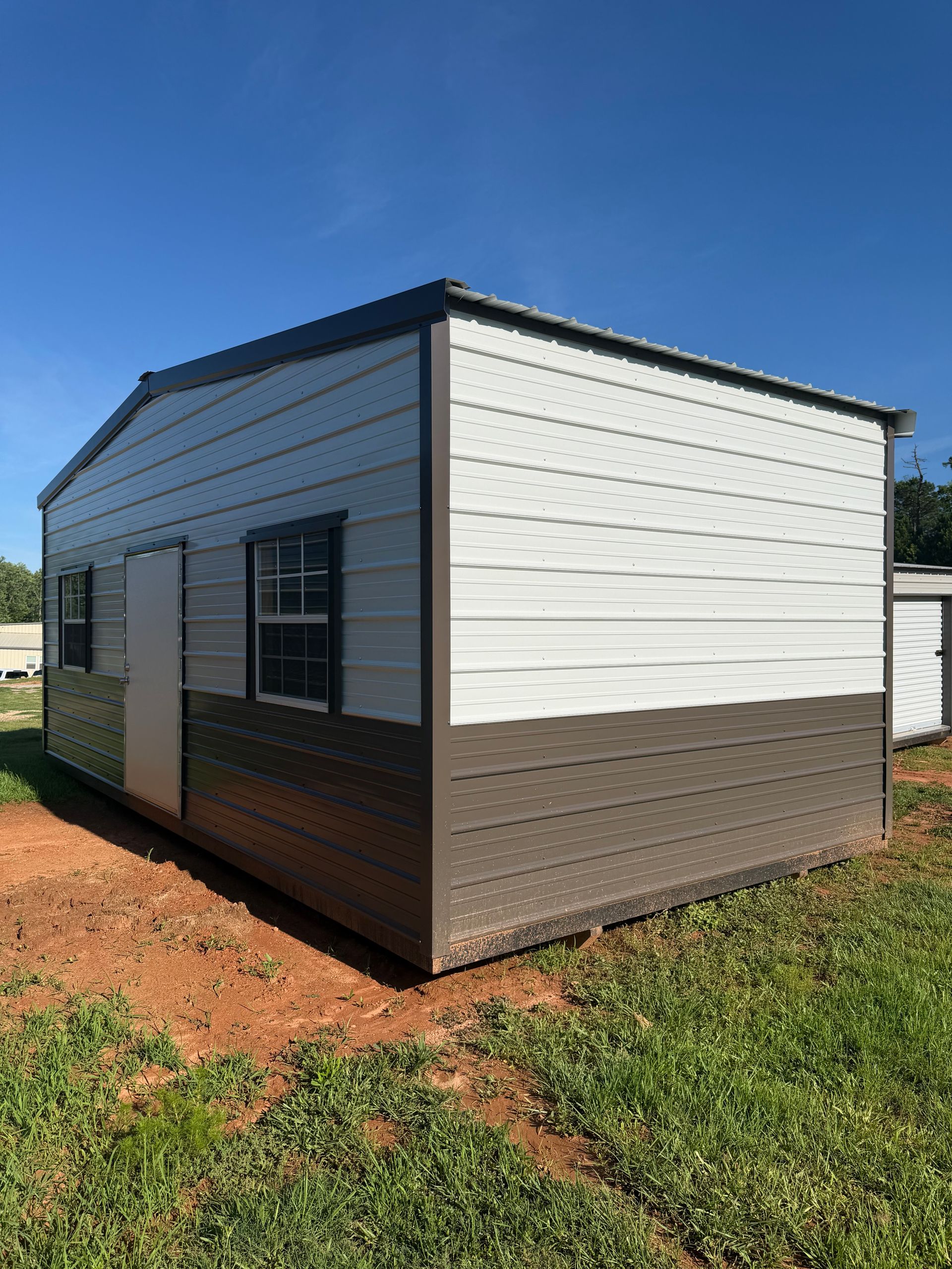 Small modern shed with white and brown siding under a clear blue sky.