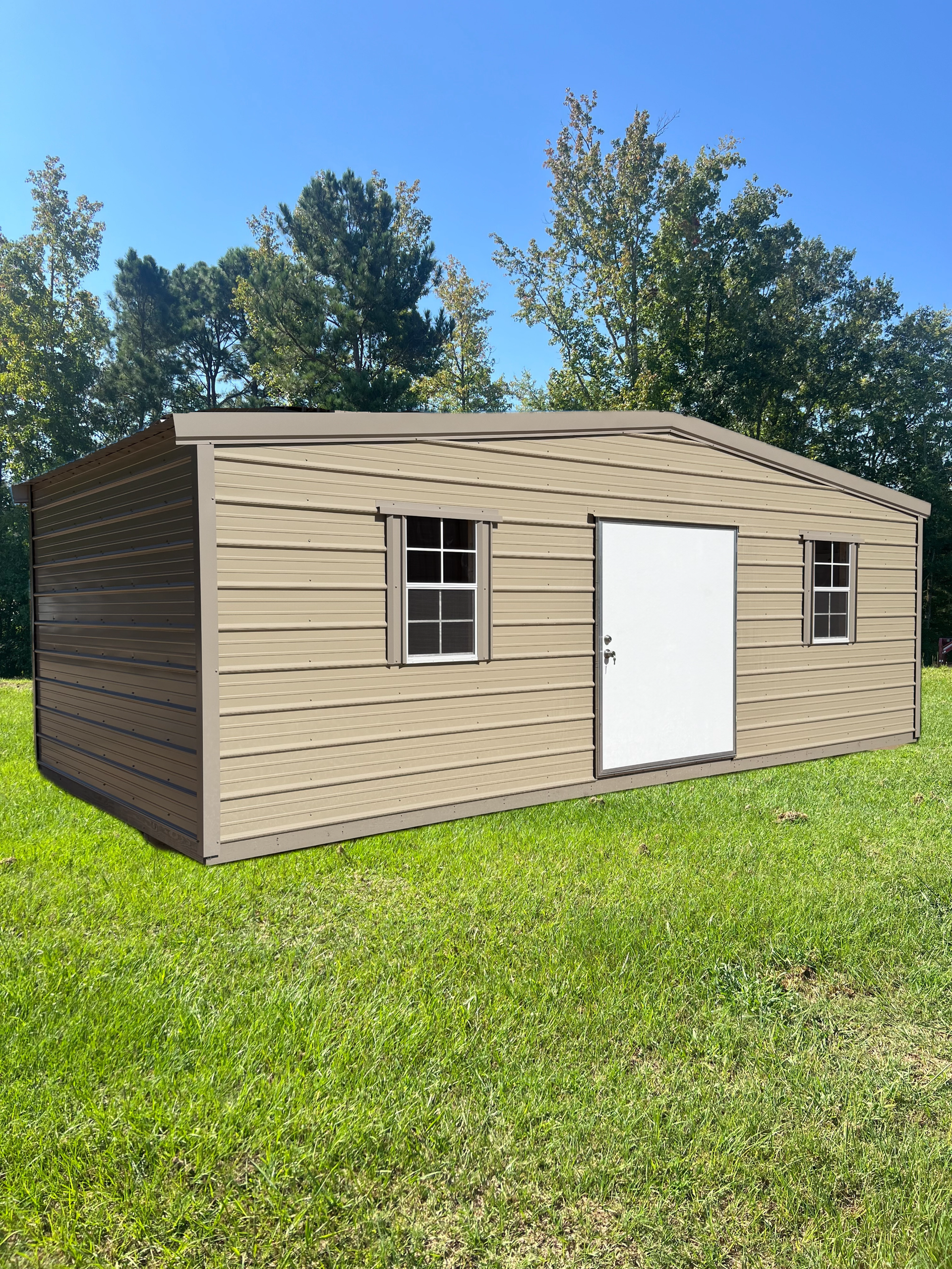 Small beige prefabricated shed with white door and windows on a grassy lawn under a blue sky.