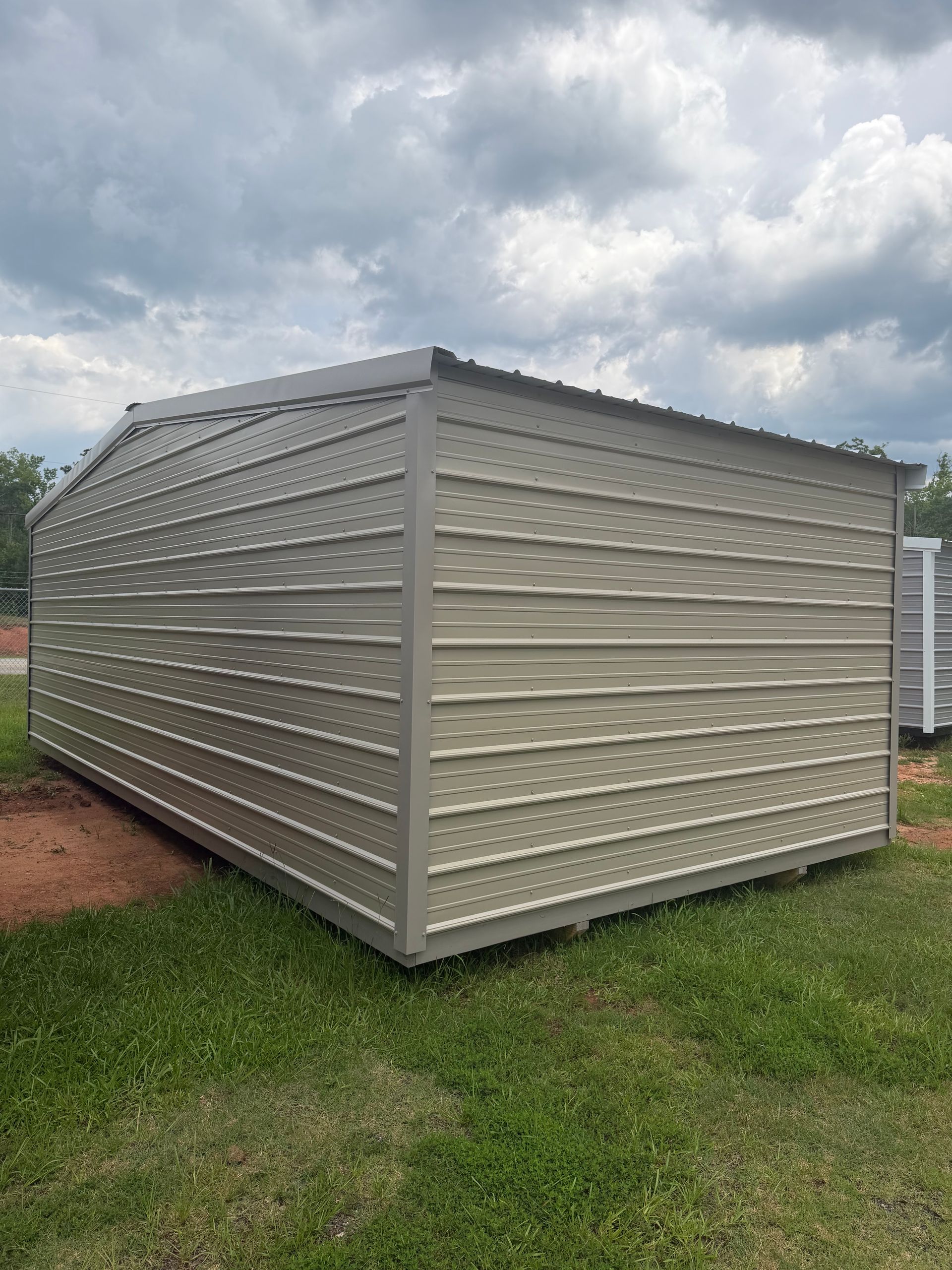 Beige metal storage shed with ribbed siding on a grassy lot under cloudy skies