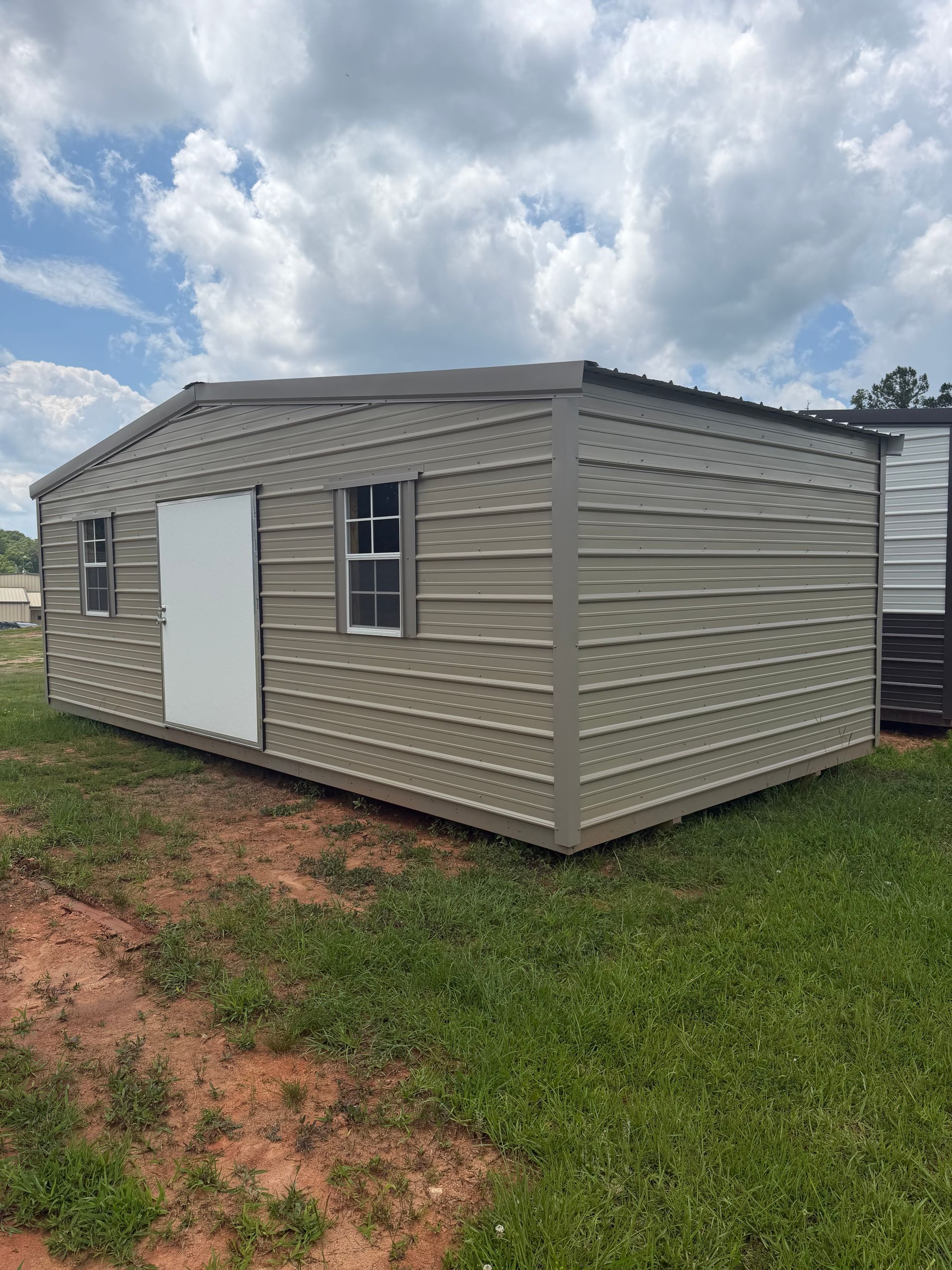 Small beige metal shed with white door and window on grass under a cloudy sky