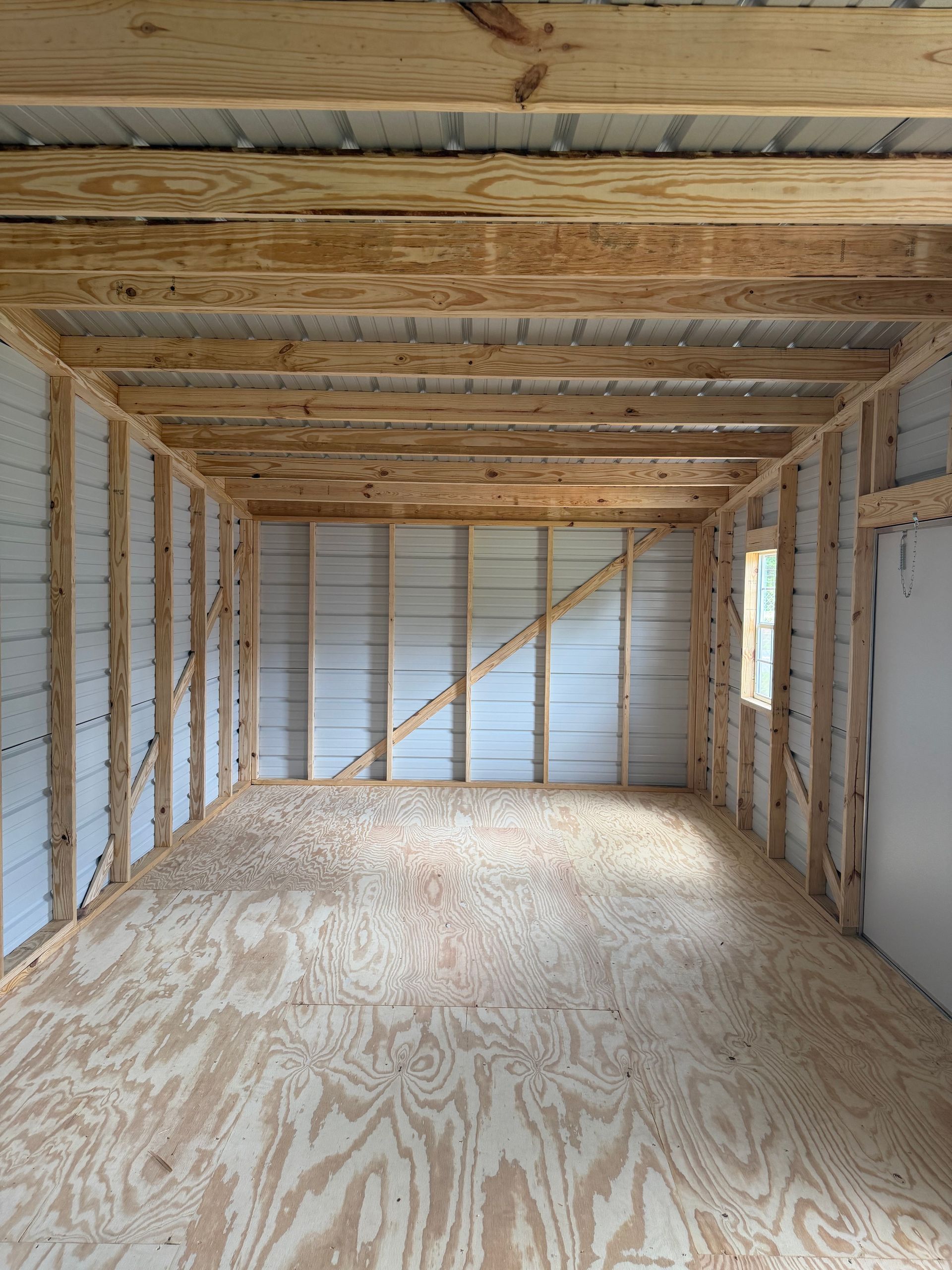 Empty unfinished room with exposed wooden framing, plywood floor, and white insulated walls.