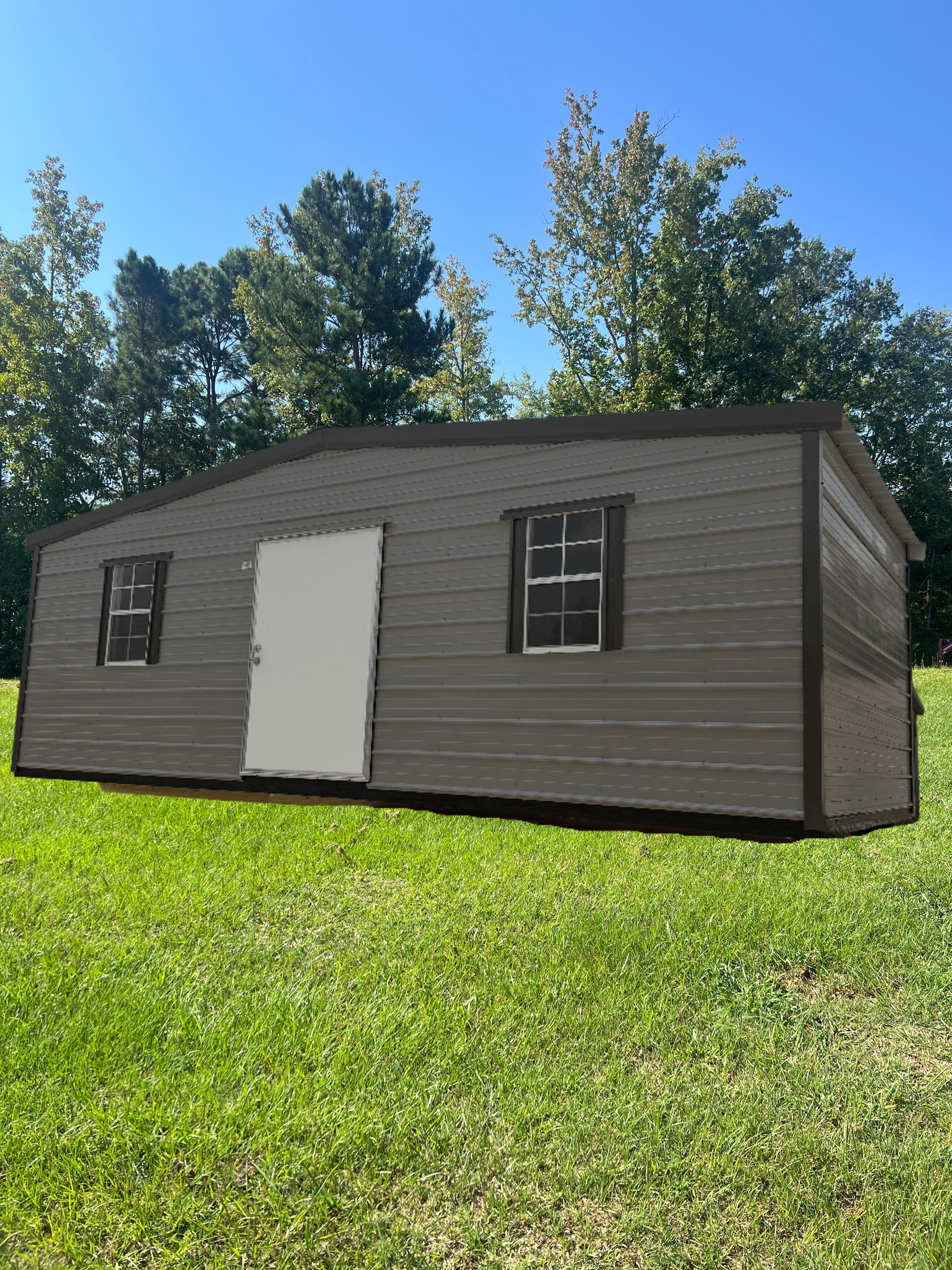Small brown shed with a white door and windows on a grassy hill under a blue sky.