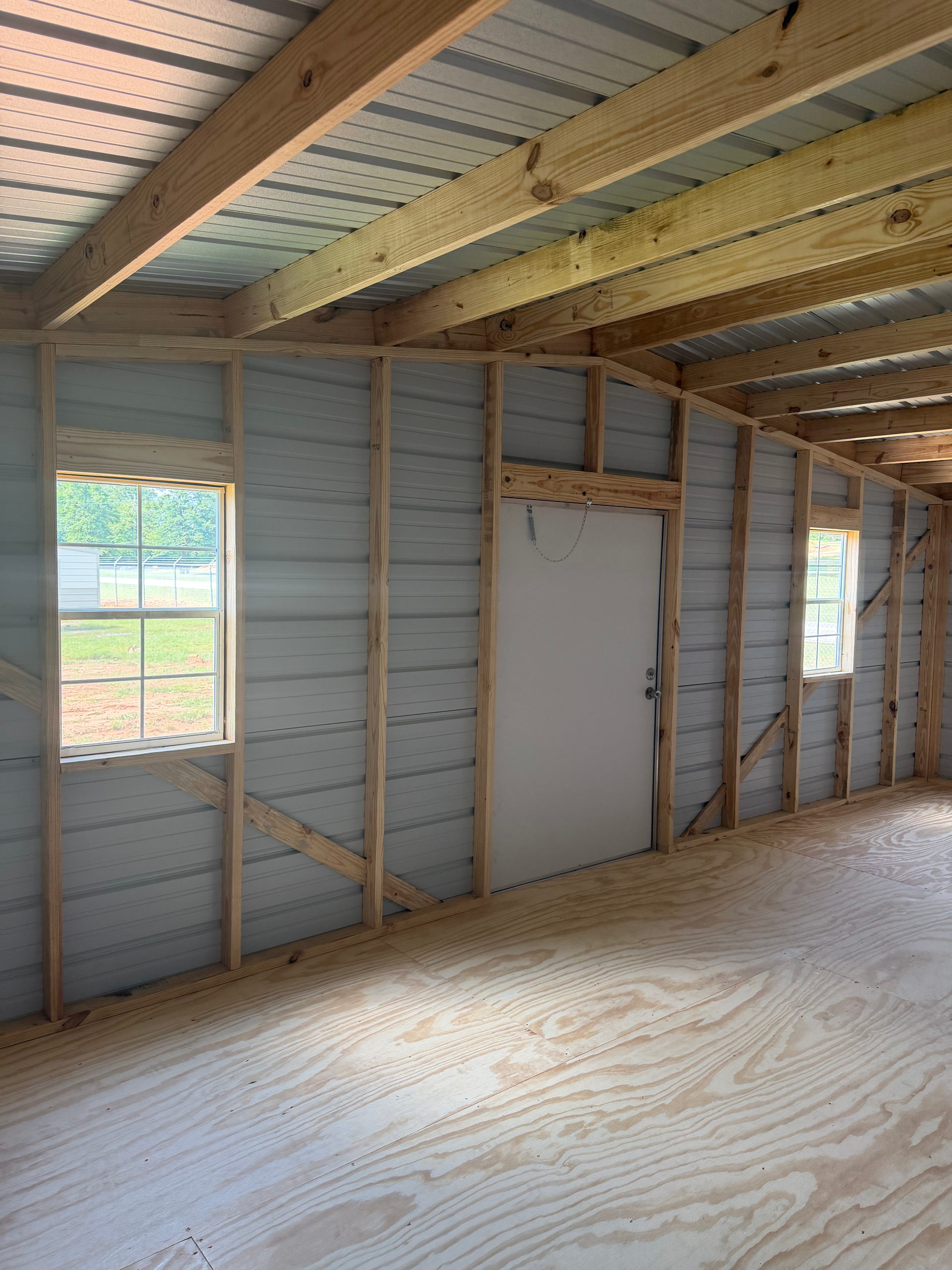 Interior of an unfinished wooden room with exposed studs, a white door, and windows.