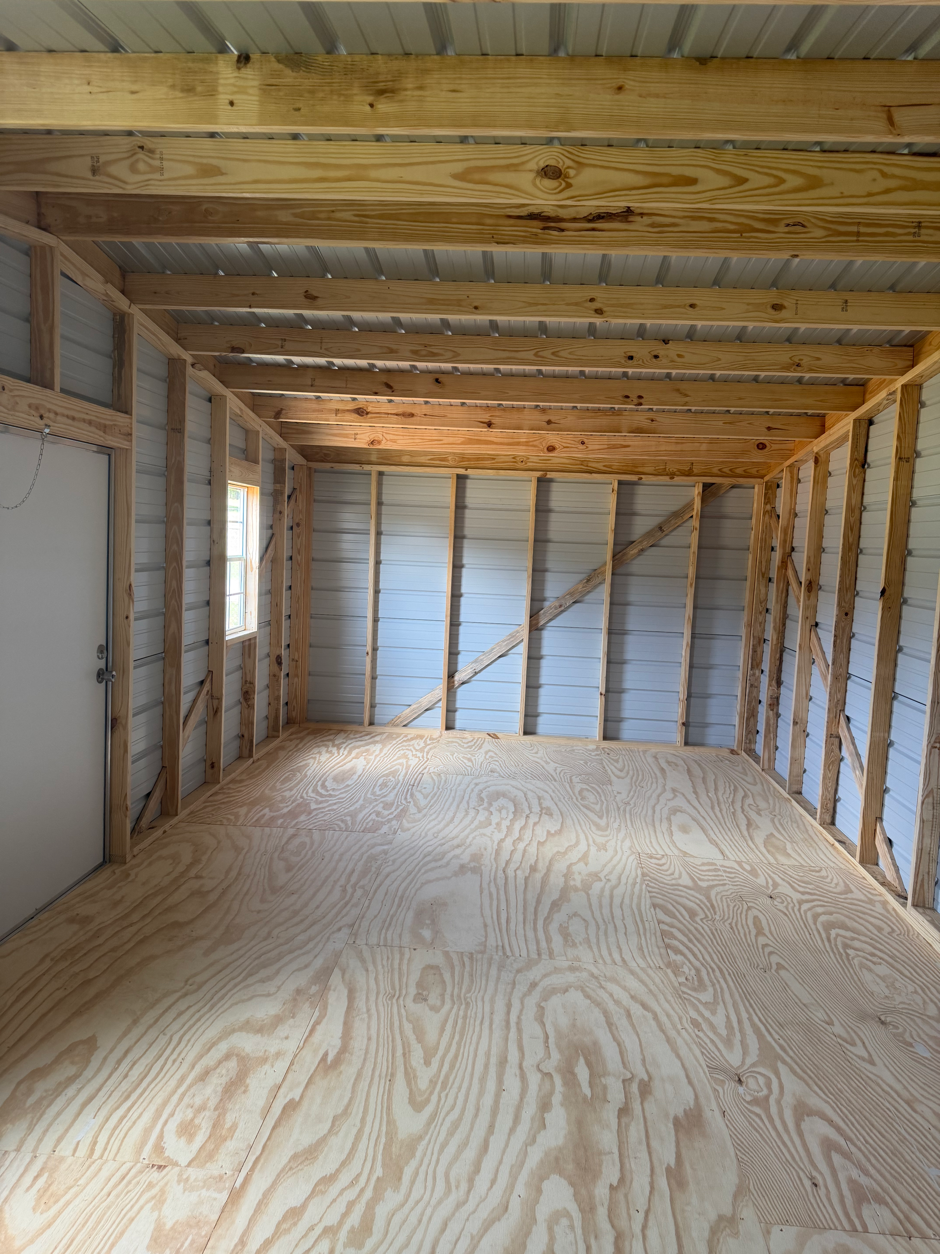 Empty unfinished room with plywood floor, exposed wood studs, and a low beam ceiling.