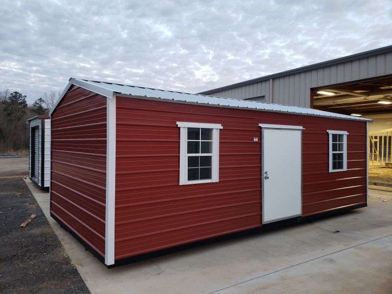 Red metal shed with white trim, two windows, and a door, set in an outdoor industrial area.