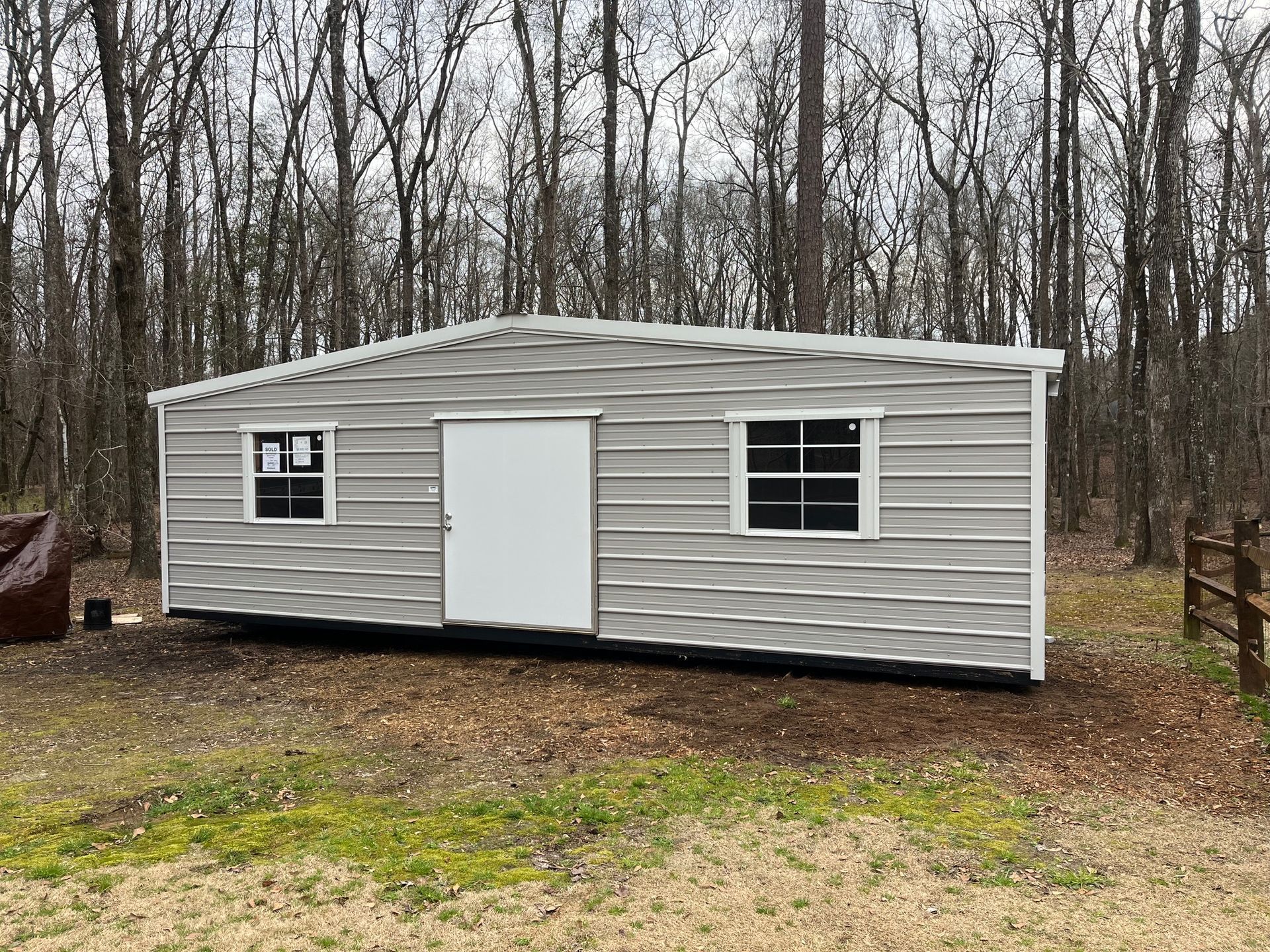 Metal shed with a white door, two windows, set in a wooded area.