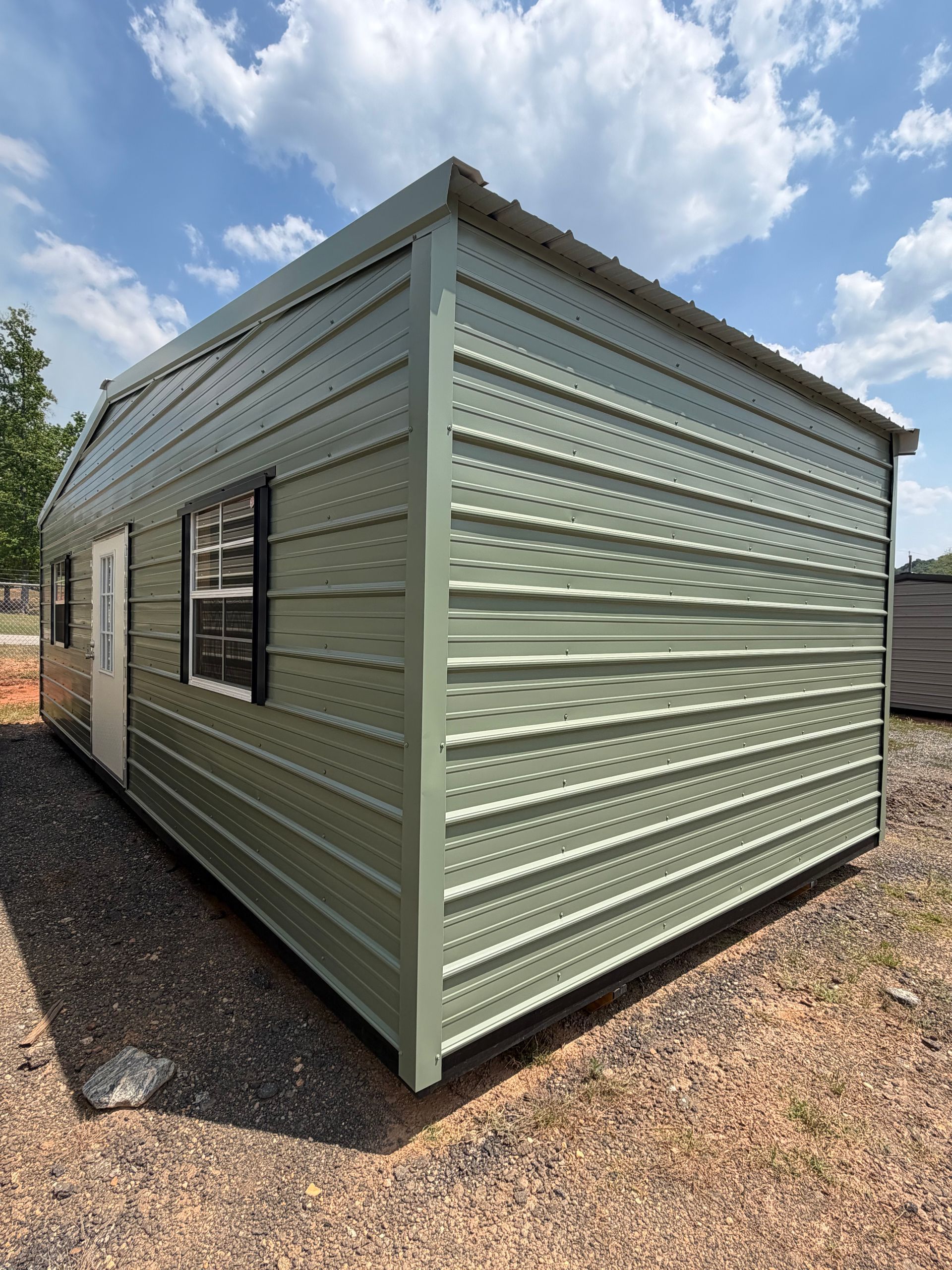 Light green corrugated metal shed with a window, shown on gravel under a blue sky