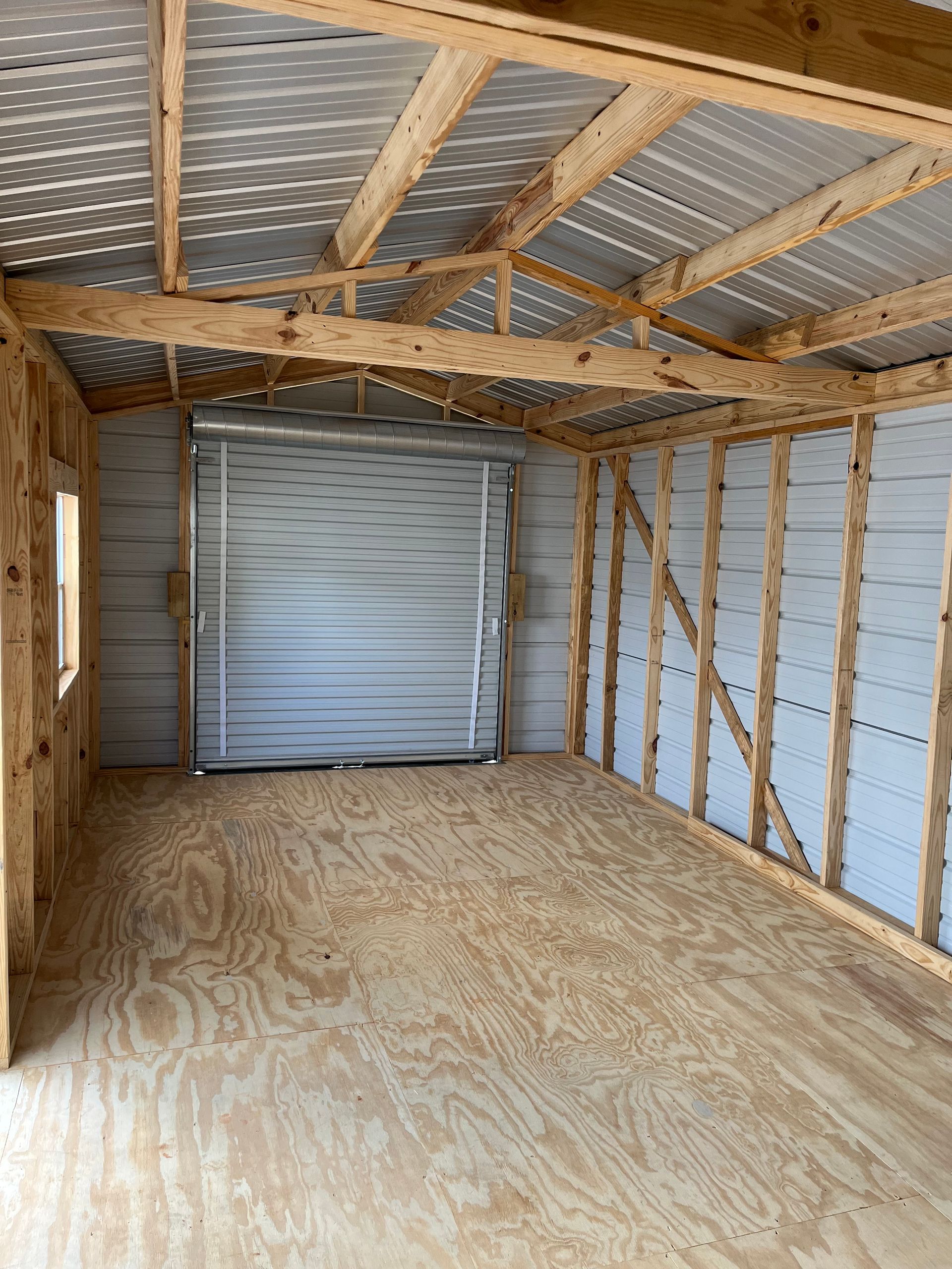 Empty unfinished garage with plywood floor, exposed framing, and a closed roll-up door