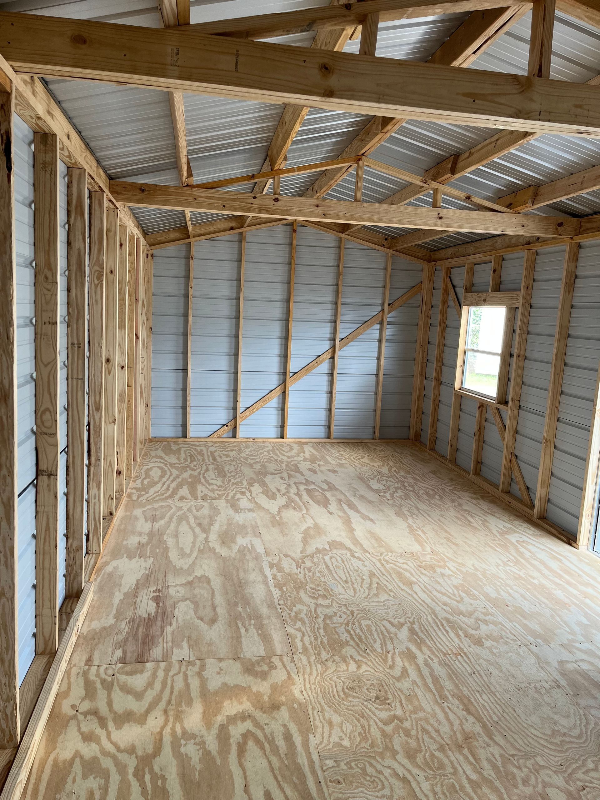 Empty framed room with plywood floor, exposed wood beams, and unfinished insulation walls