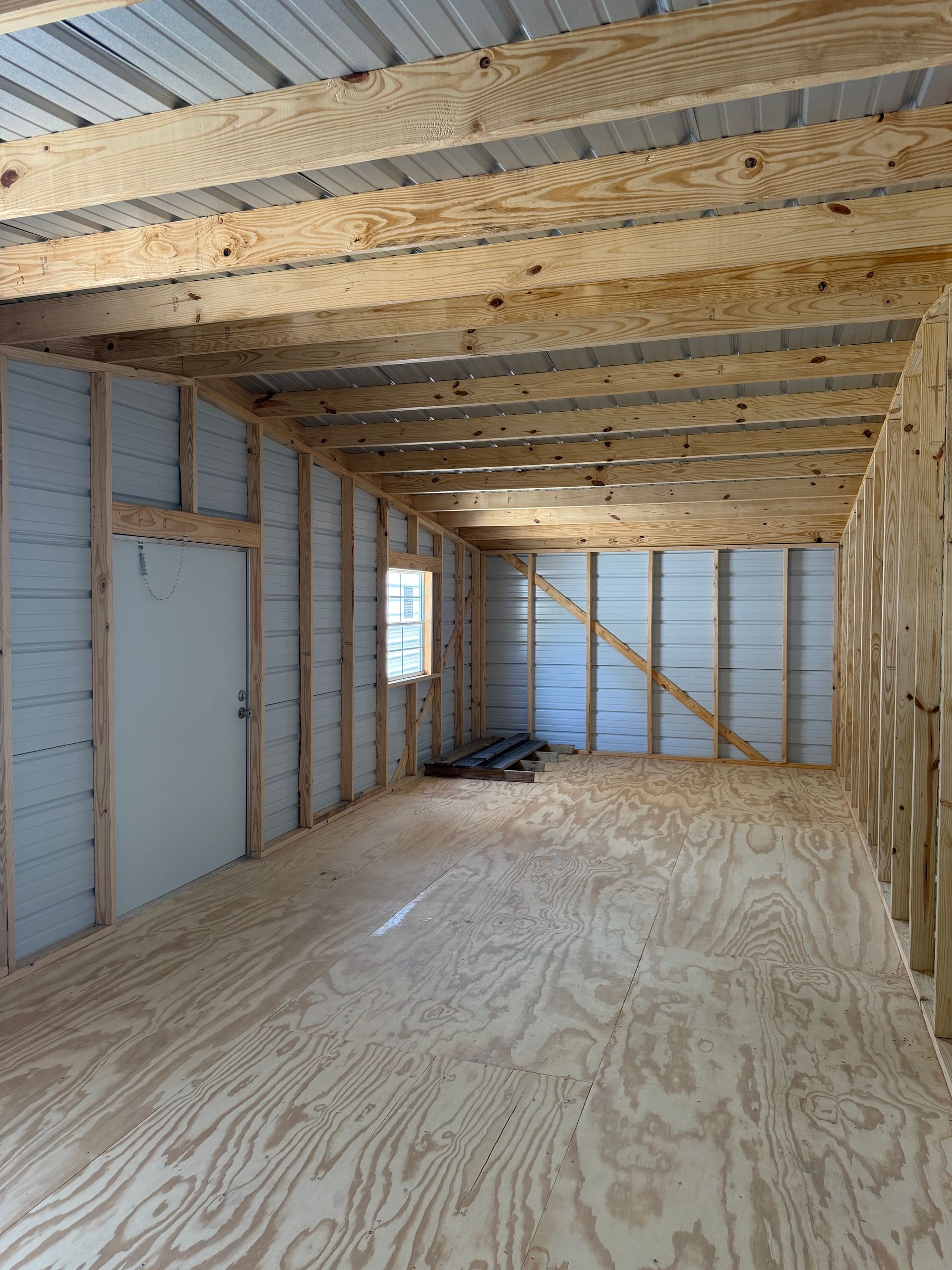 Unfinished room with plywood floor, exposed wood framing, insulated walls, and small window.
