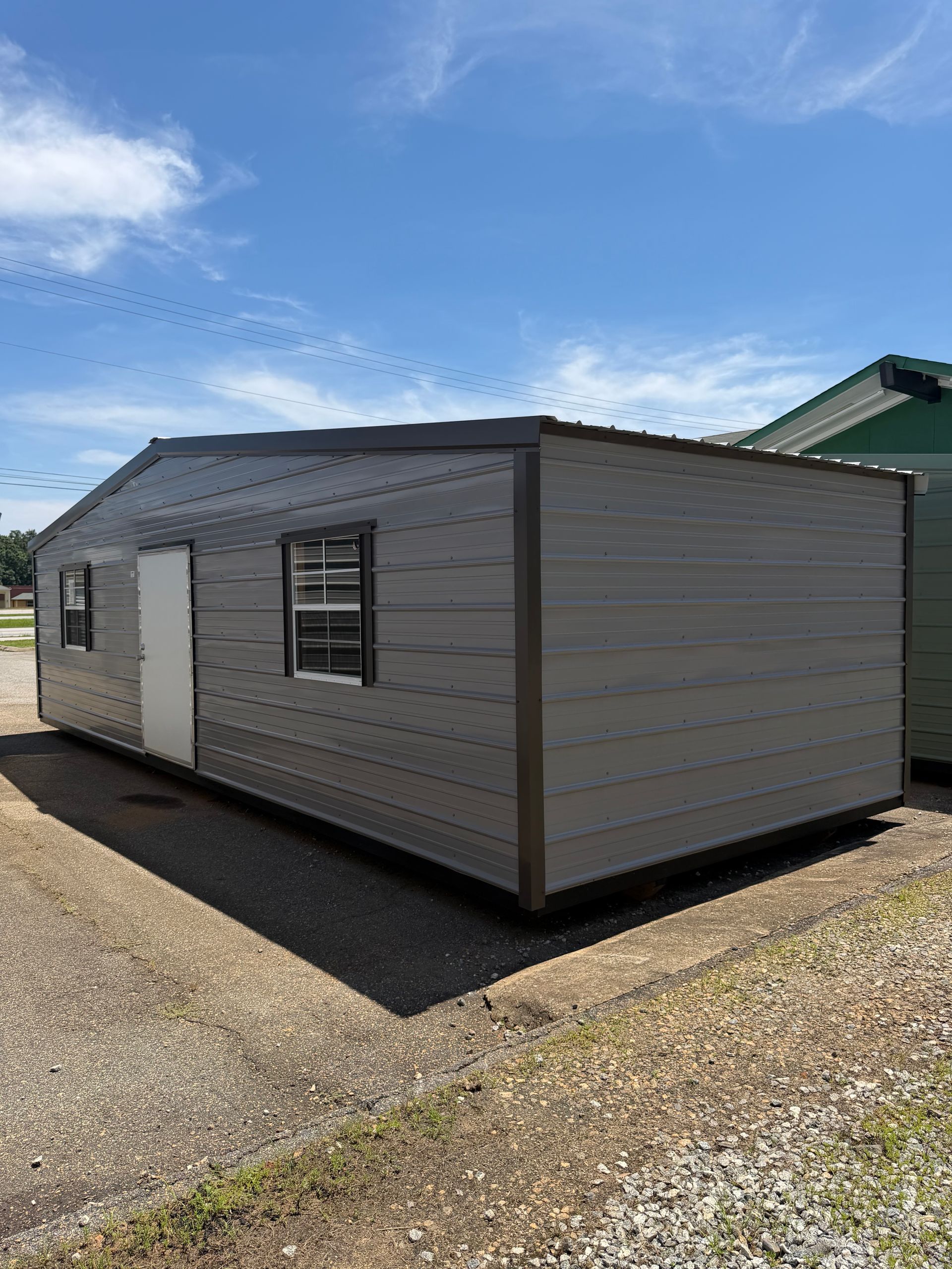 Gray mobile home on a gravel lot under a blue sky