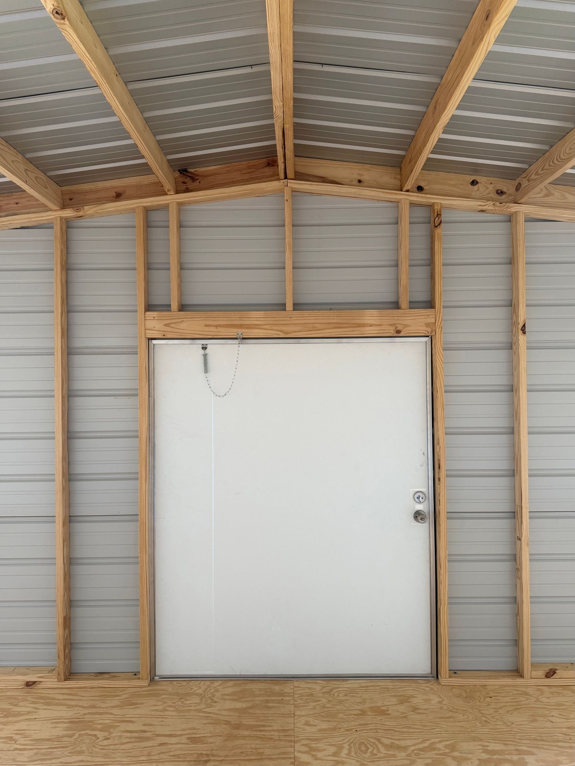 White door in a wooden-framed shed with metal siding and corrugated roof panels