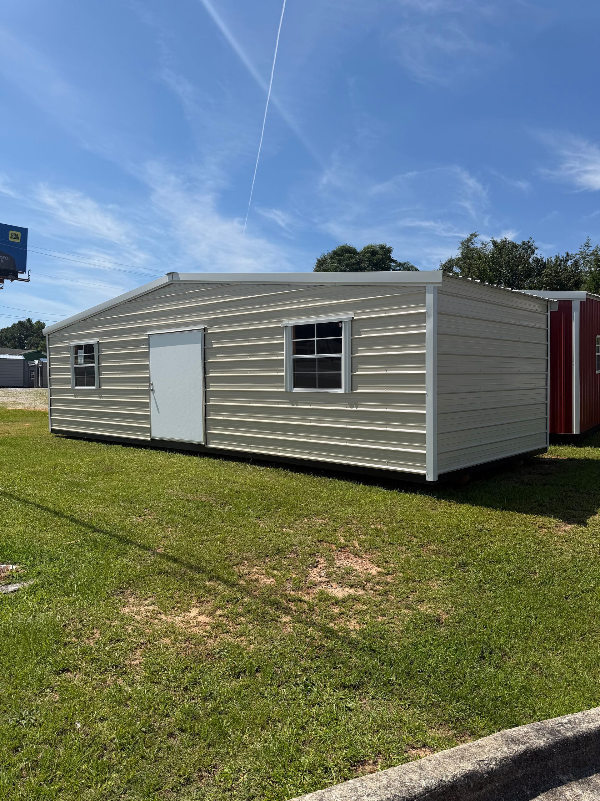 White portable building on a grassy lot under a blue sky, with a white door and window.