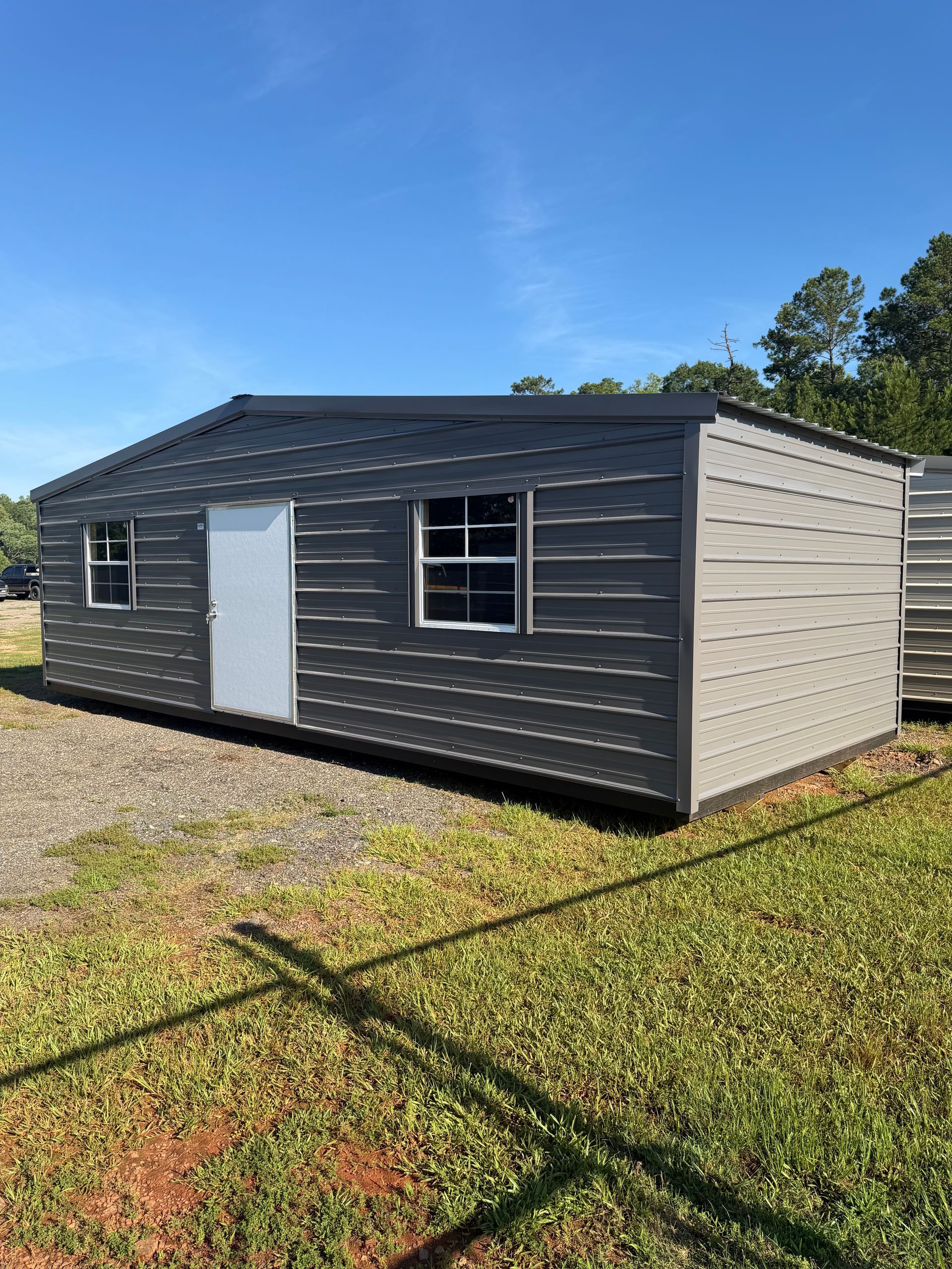 Gray mobile home with white trim on a grassy lot under a clear blue sky