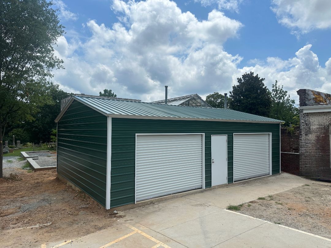 Green metal garage with two roll-up doors, a white door, and a concrete path.