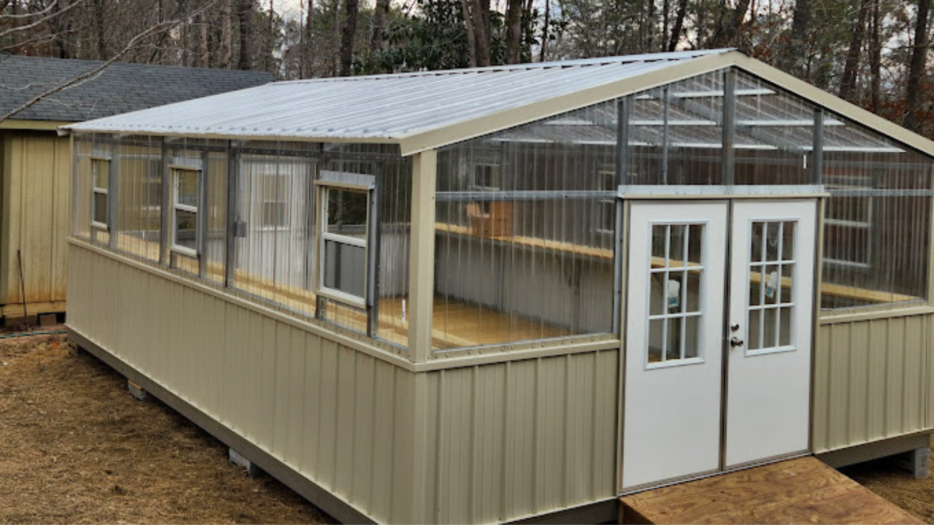Tan greenhouse with clear corrugated panels, white doors, and windows.