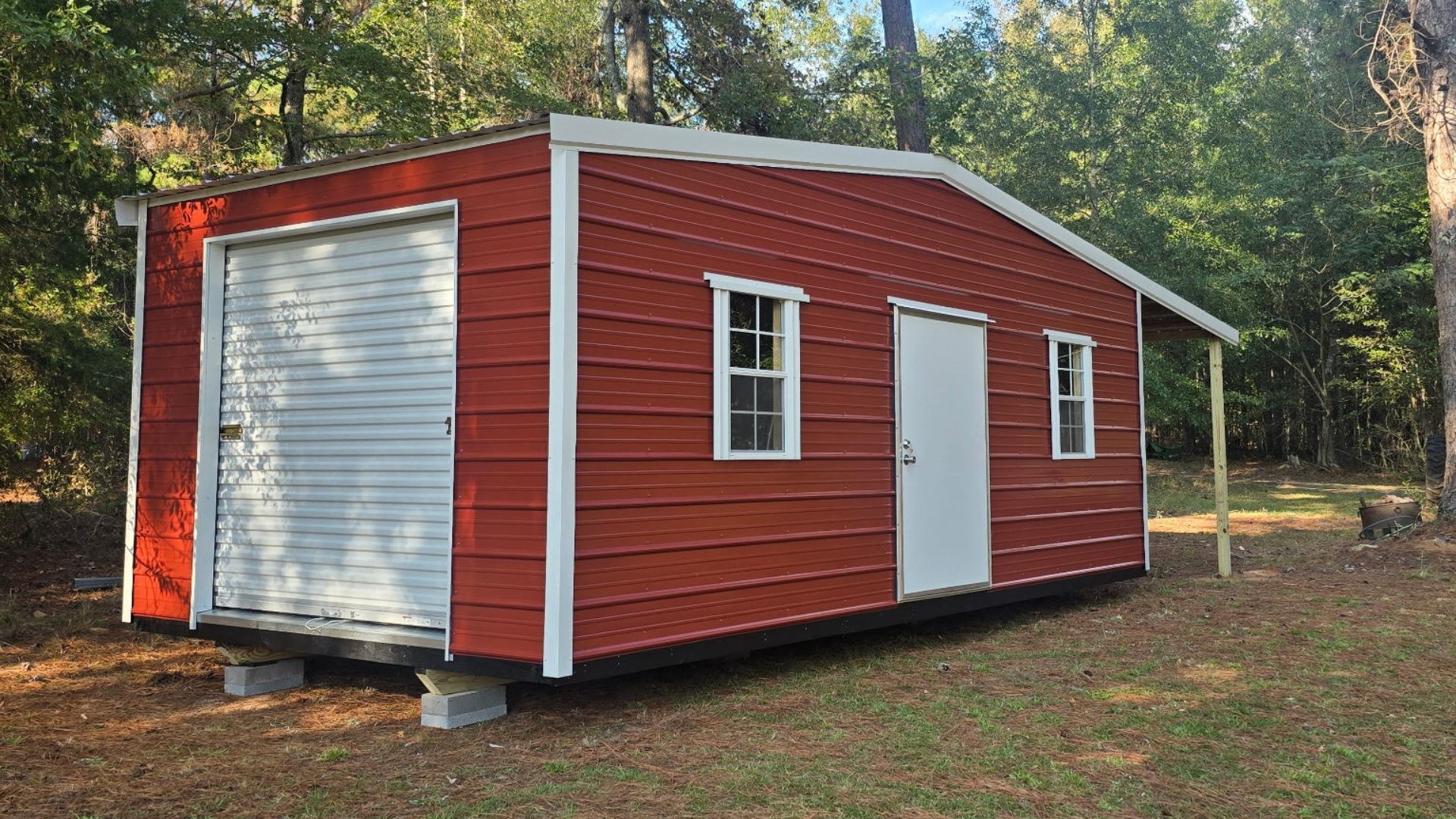 Red shed with garage door, white door, and windows in a wooded area.