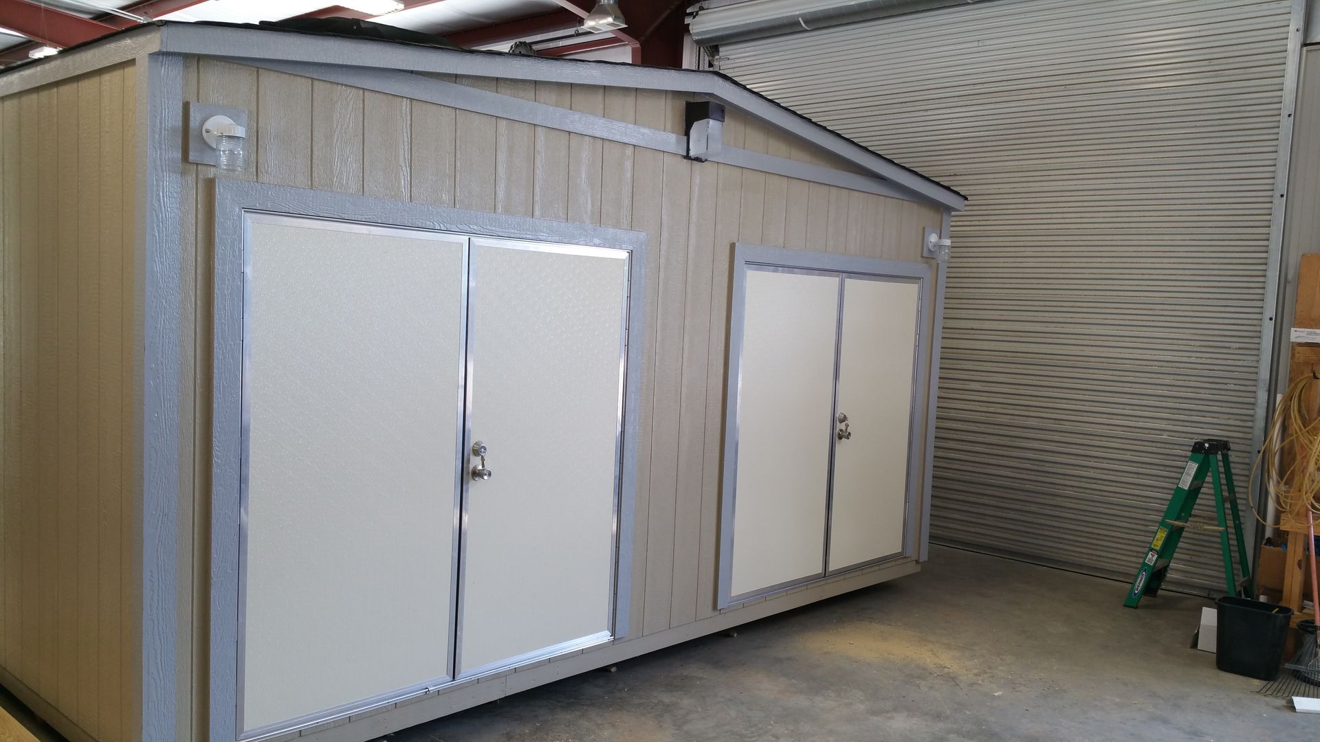A shed with white doors and a ladder in front of it.