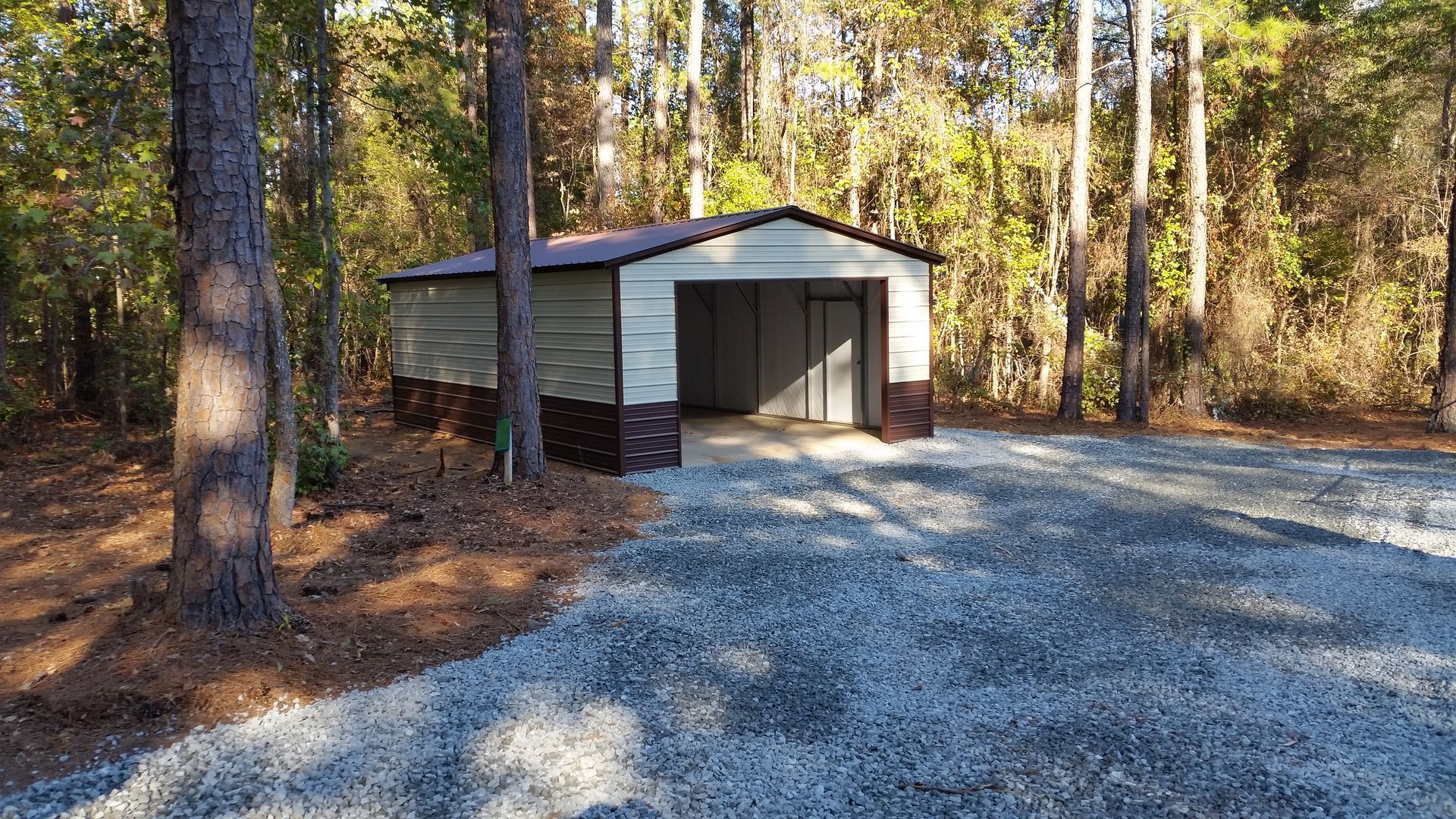 Garage building with open door, gravel driveway, and trees.