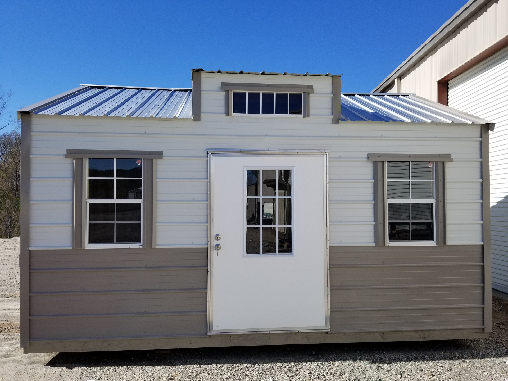Small tan house with white trim, central door, and two windows under a metal roof.