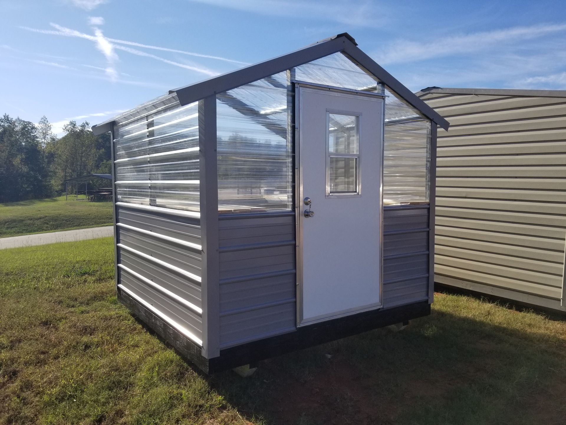 A small greenhouse with a white door is sitting in the middle of a grassy field.