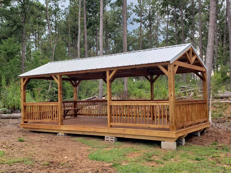 Wooden pavilion with a metal roof in a wooded area.