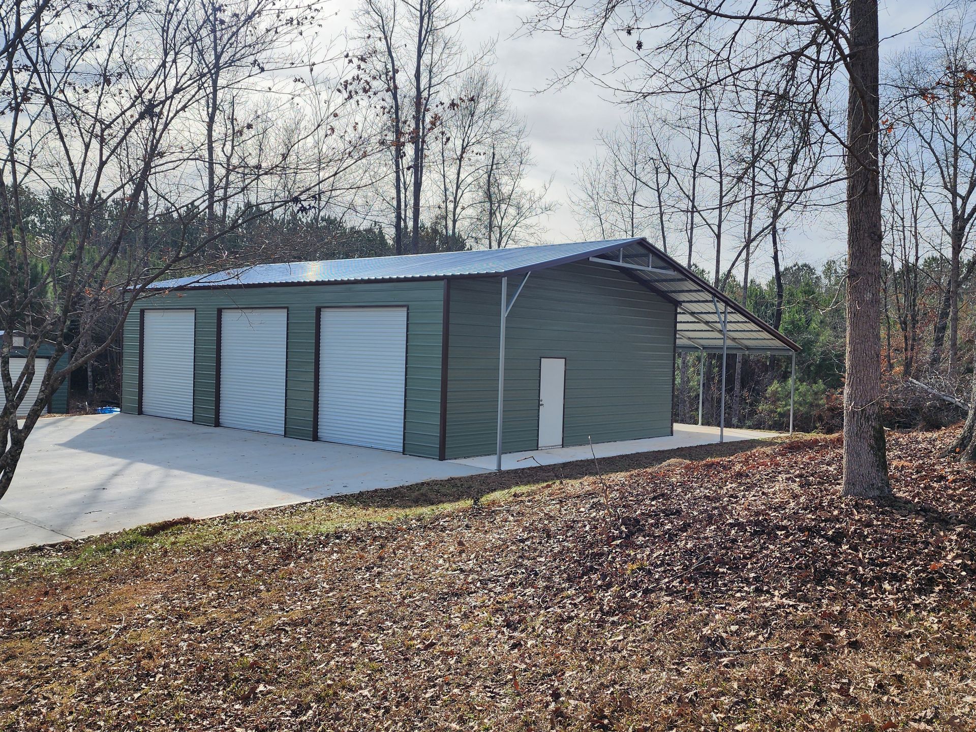 A green garage with white doors is surrounded by trees and leaves.
