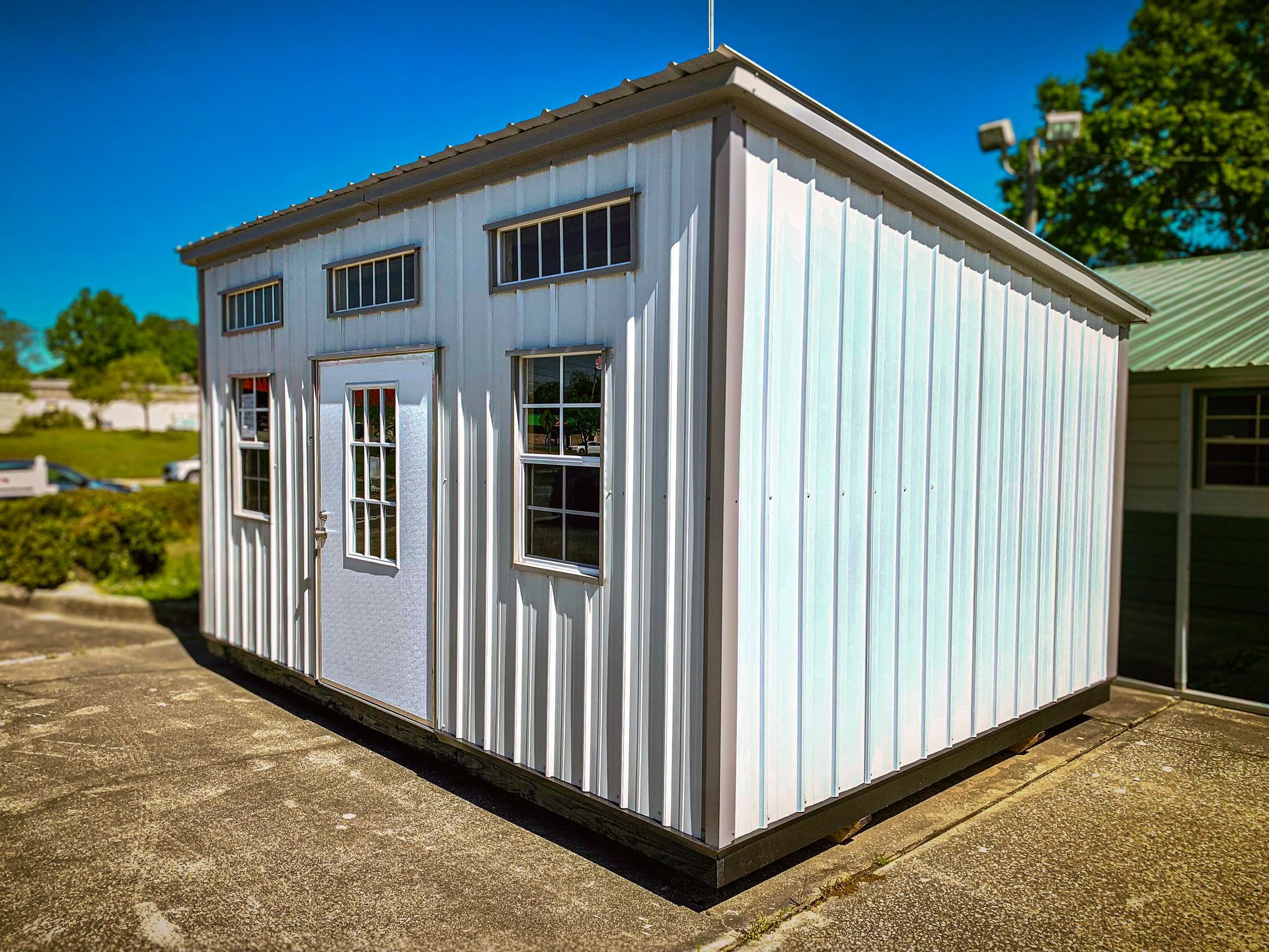 A small white shed with a green roof is sitting in a parking lot.