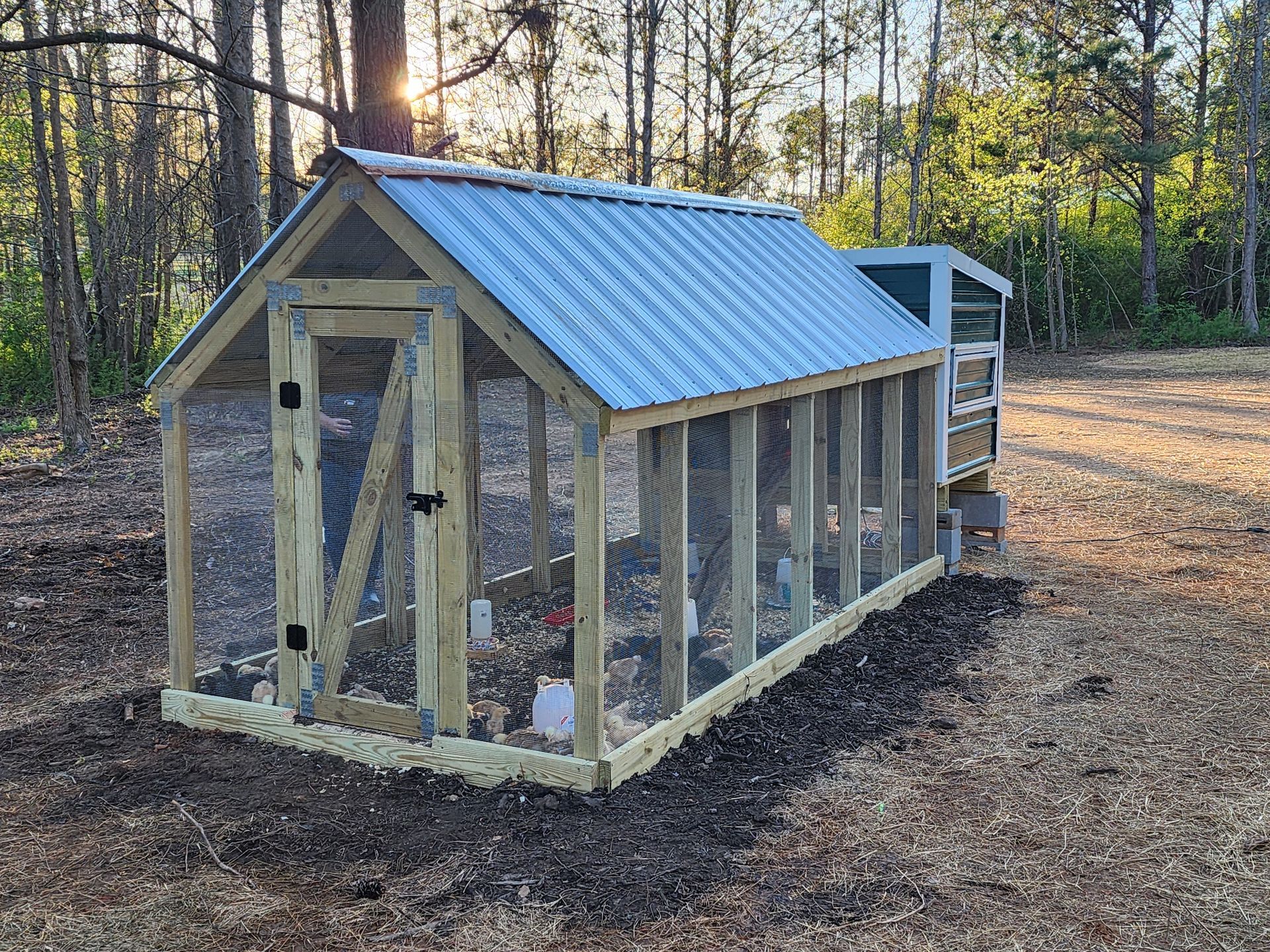 A wooden chicken coop with a metal roof is sitting in the middle of a dirt field.