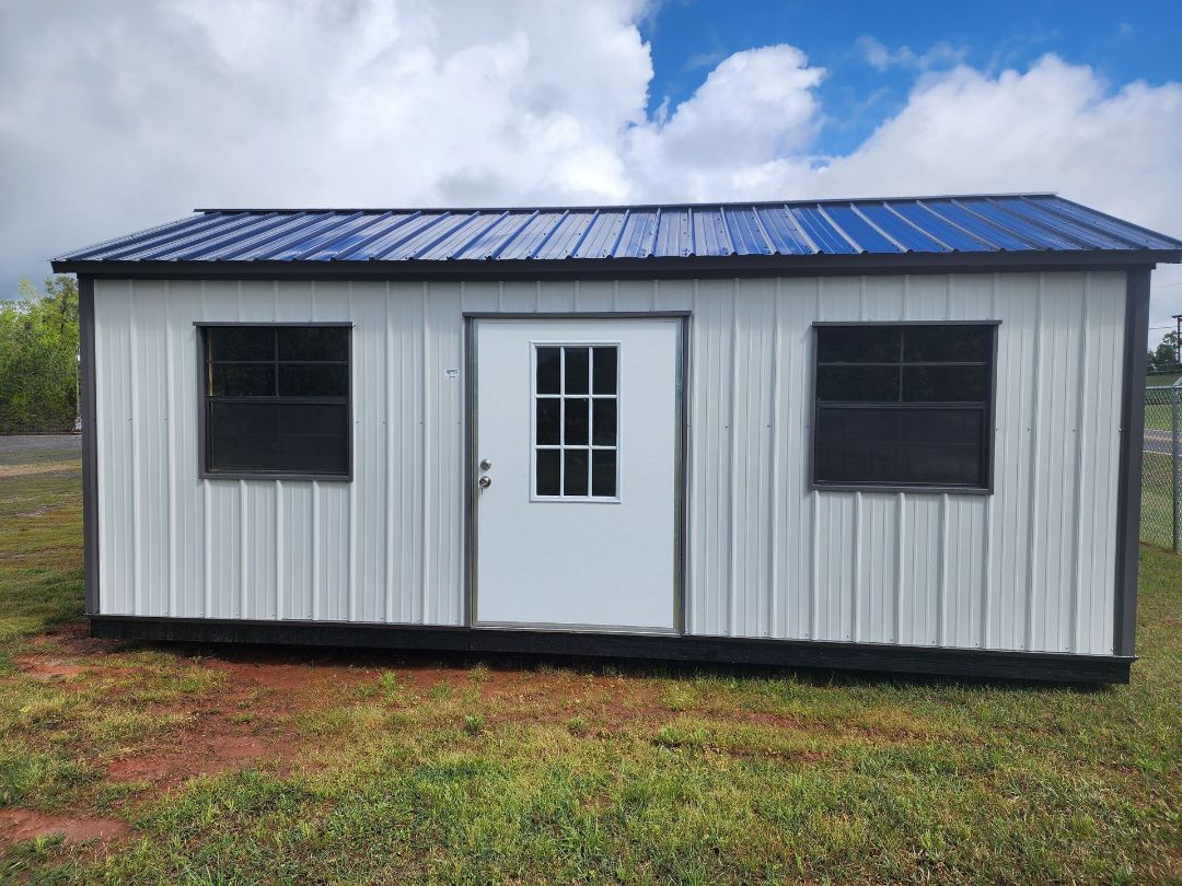 A small white building with a black roof is sitting in the middle of a grassy field.